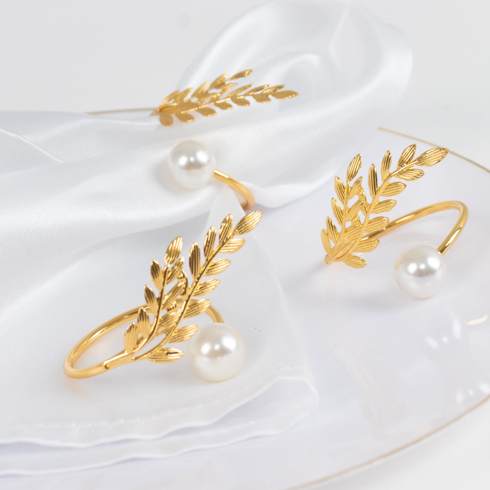 Gold leaf napkin rings with white pearl accent on a white napkin.
