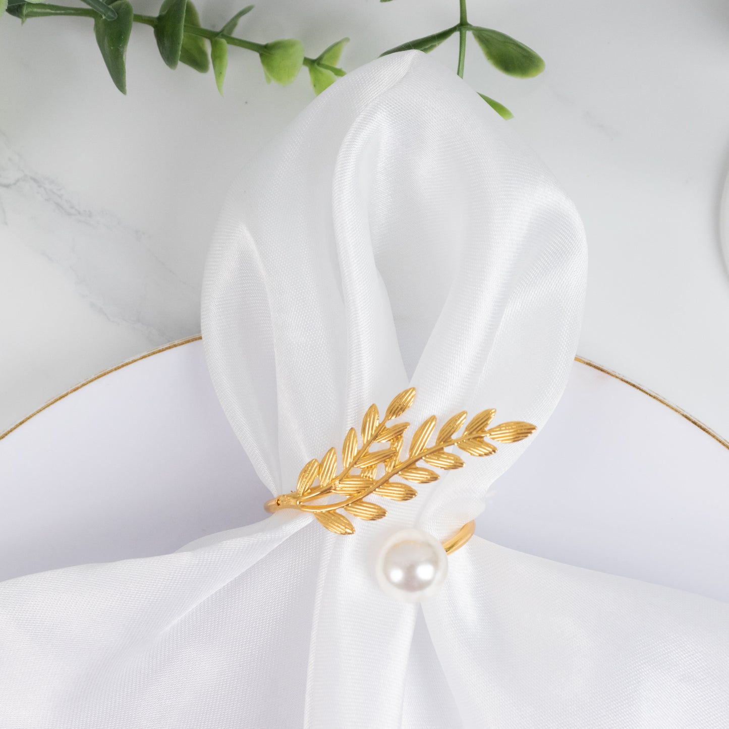 Gold leaf napkin ring with white pearl accent on a white napkin.