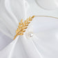 Gold leaf napkin ring with pearl accent on white fabric.