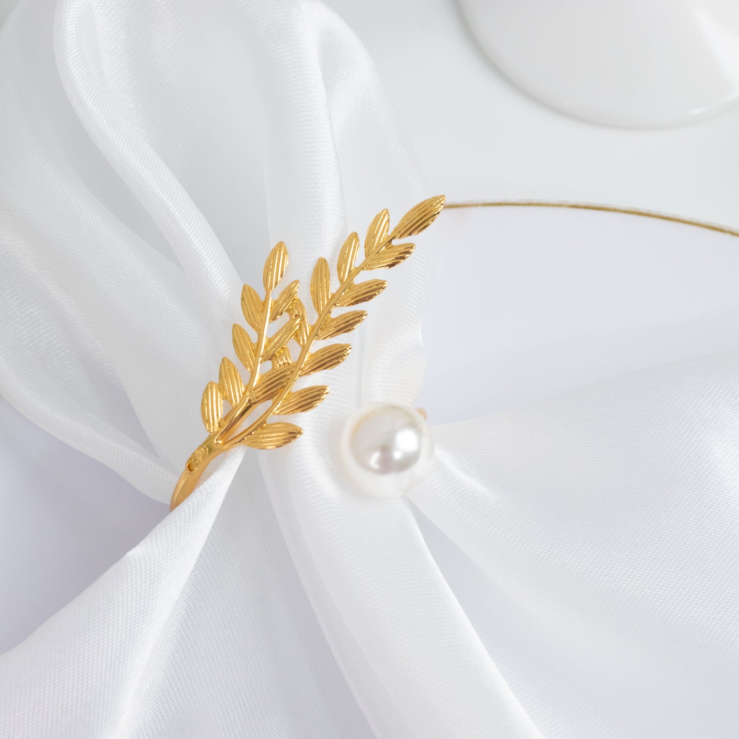 Gold leaf napkin ring with pearl accent on white fabric.