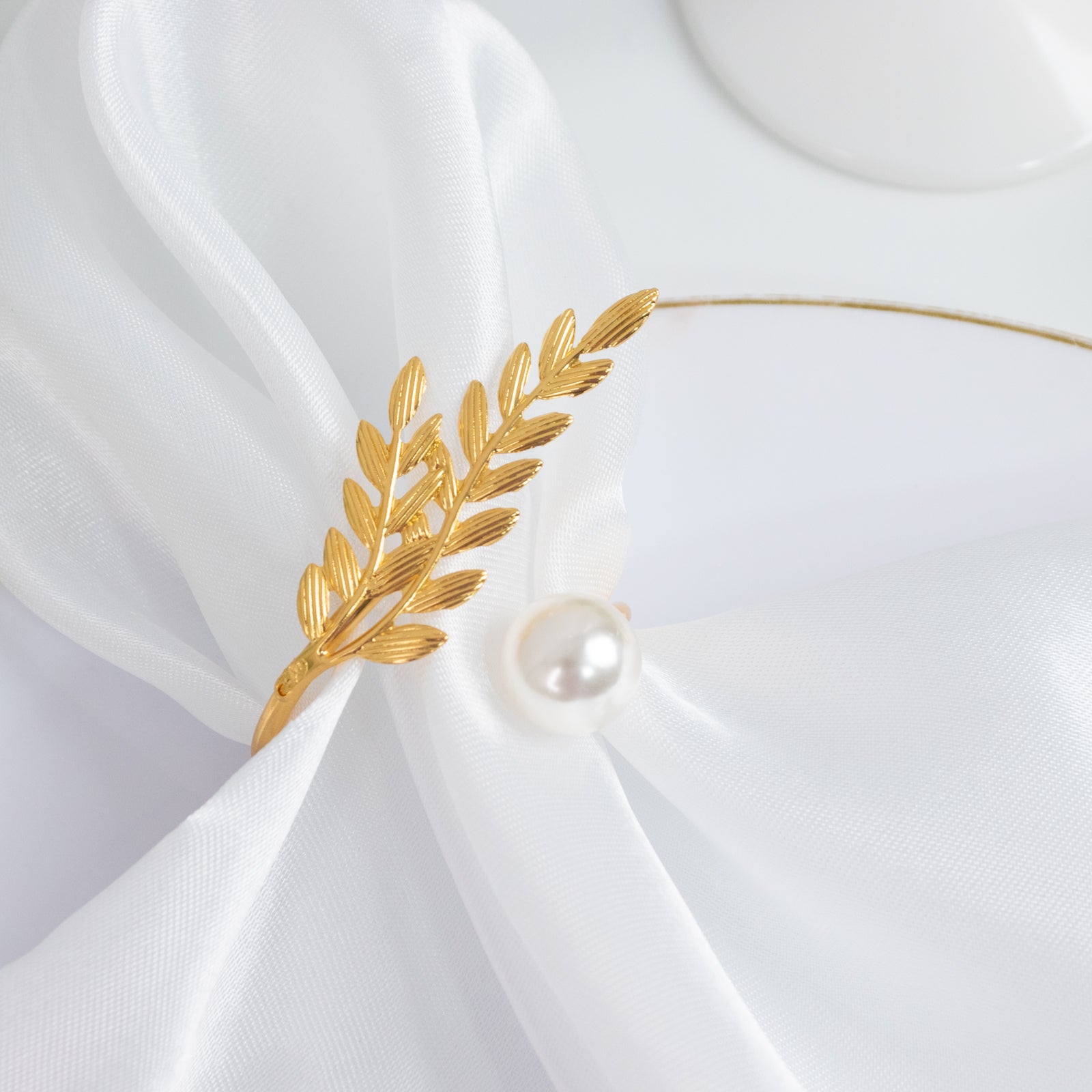 Gold leaf napkin ring with pearl accent on white fabric.