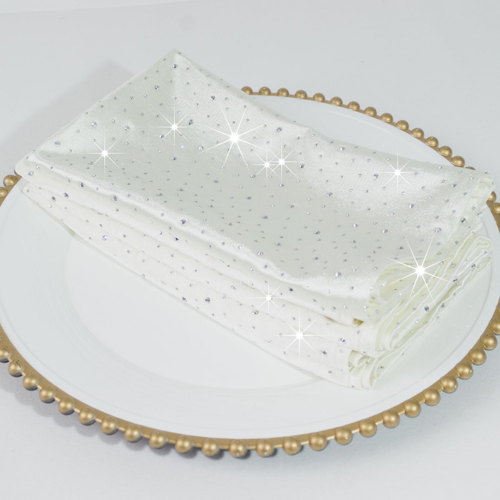 Pearl white reusable cloth napkins with rhinestone accents on a decorative plate.