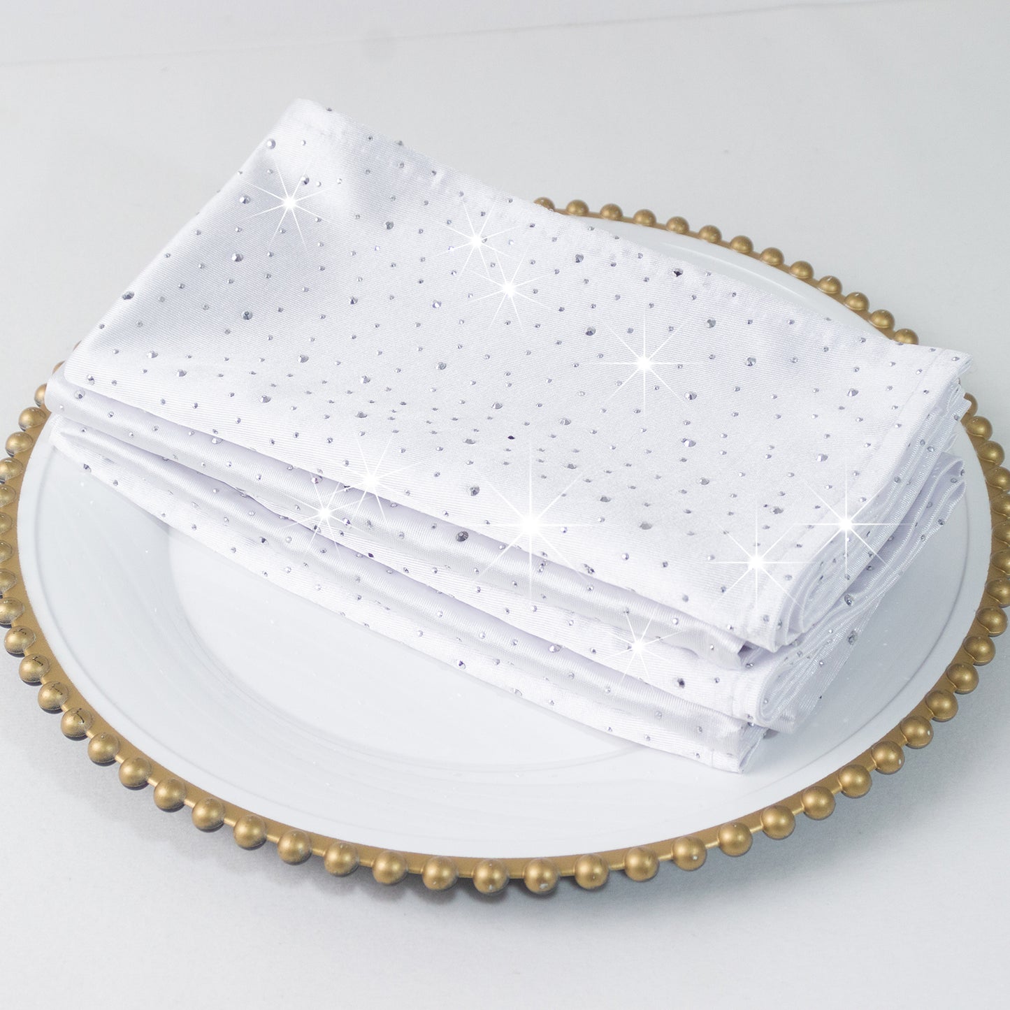 White scuba polyester napkins with rhinestone accents on a decorative plate.