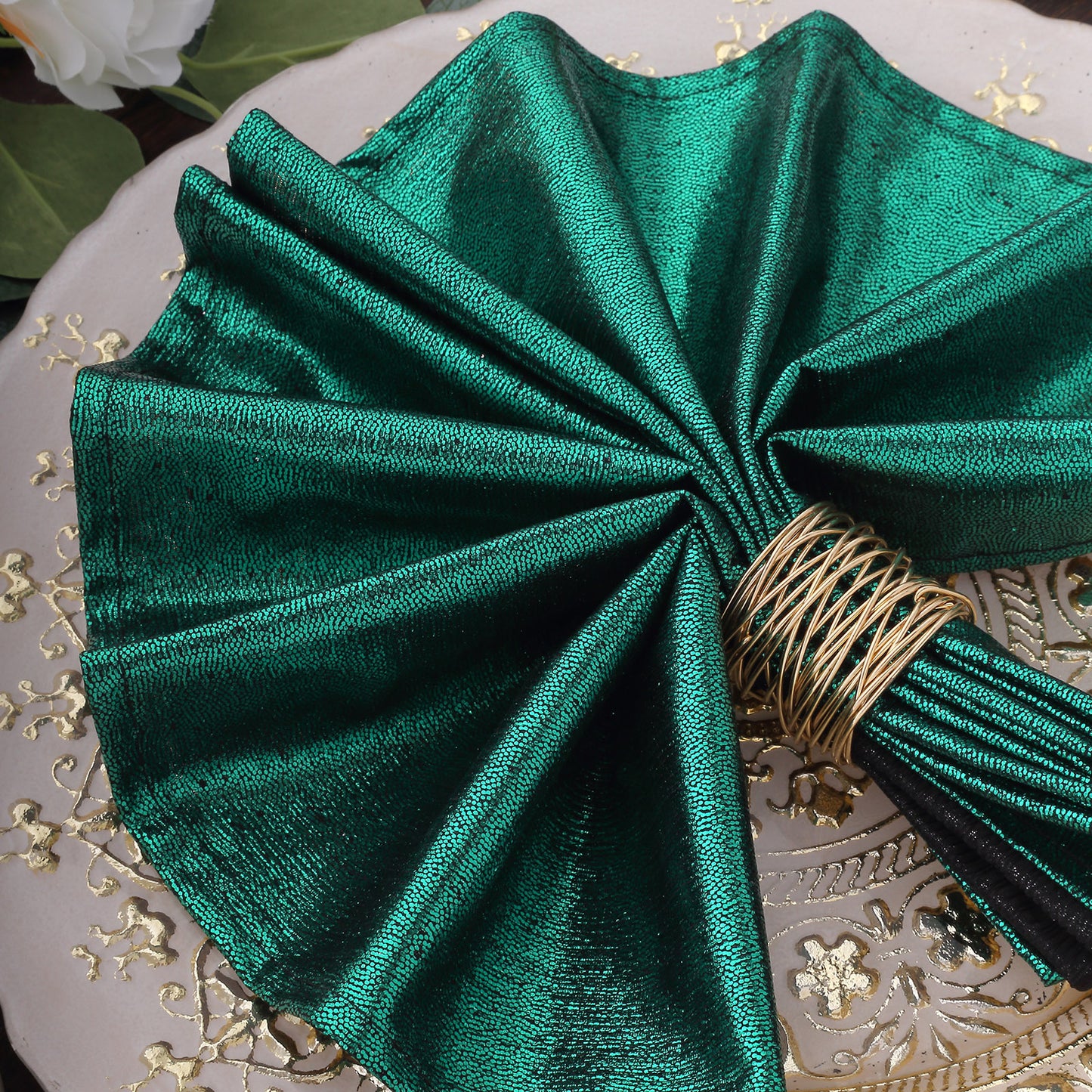 Emerald green shimmer sequin table napkin elegantly folded on a decorative plate.