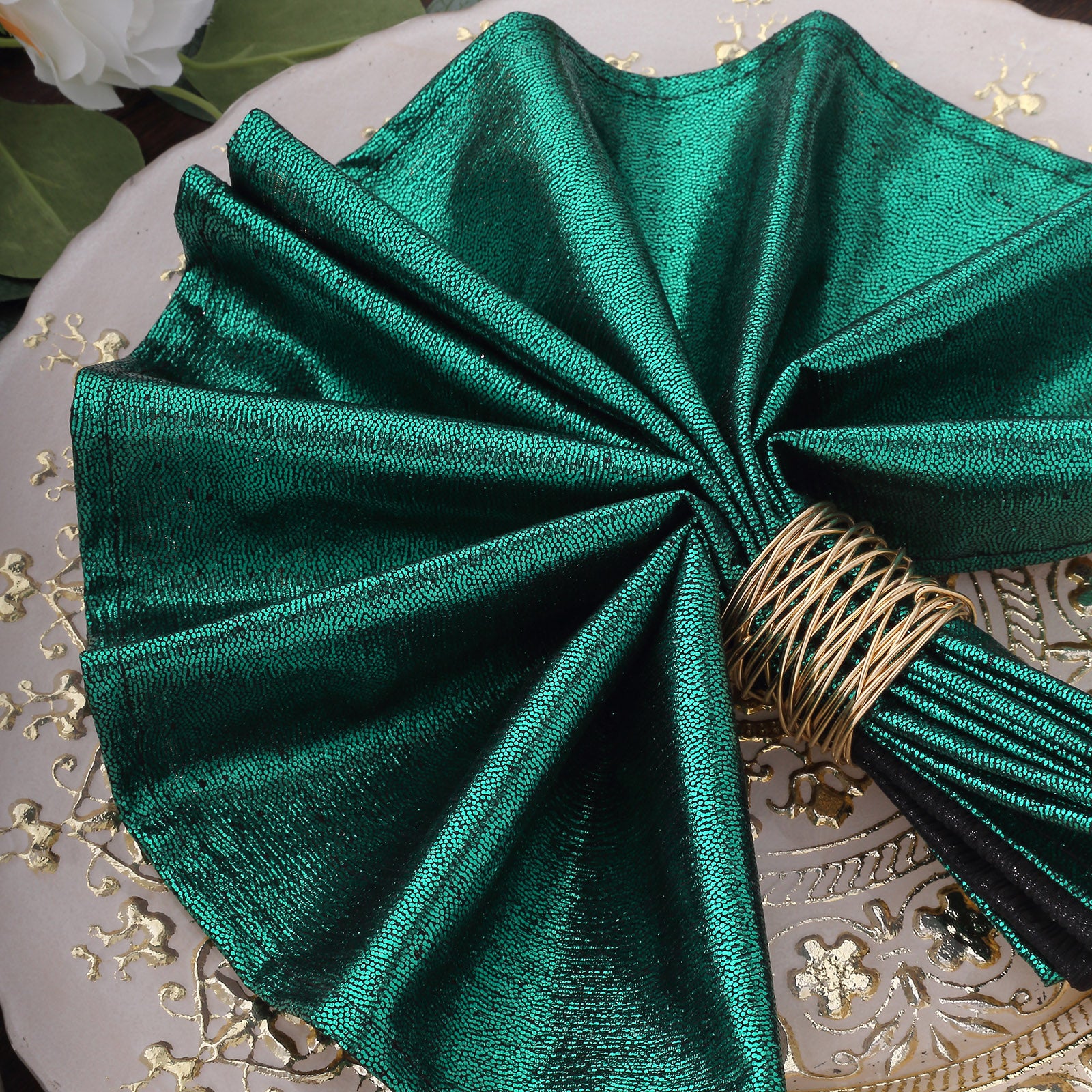 Emerald green shimmer sequin table napkin elegantly folded on a decorative plate.