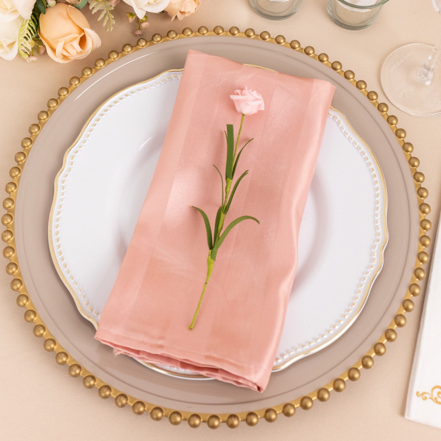 Dusty rose satin linen napkin with a flower, elegantly placed on a decorated plate.