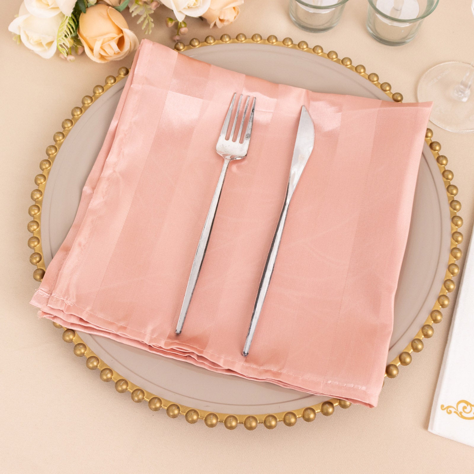 Dusty rose striped satin linen napkin on a decorative plate.