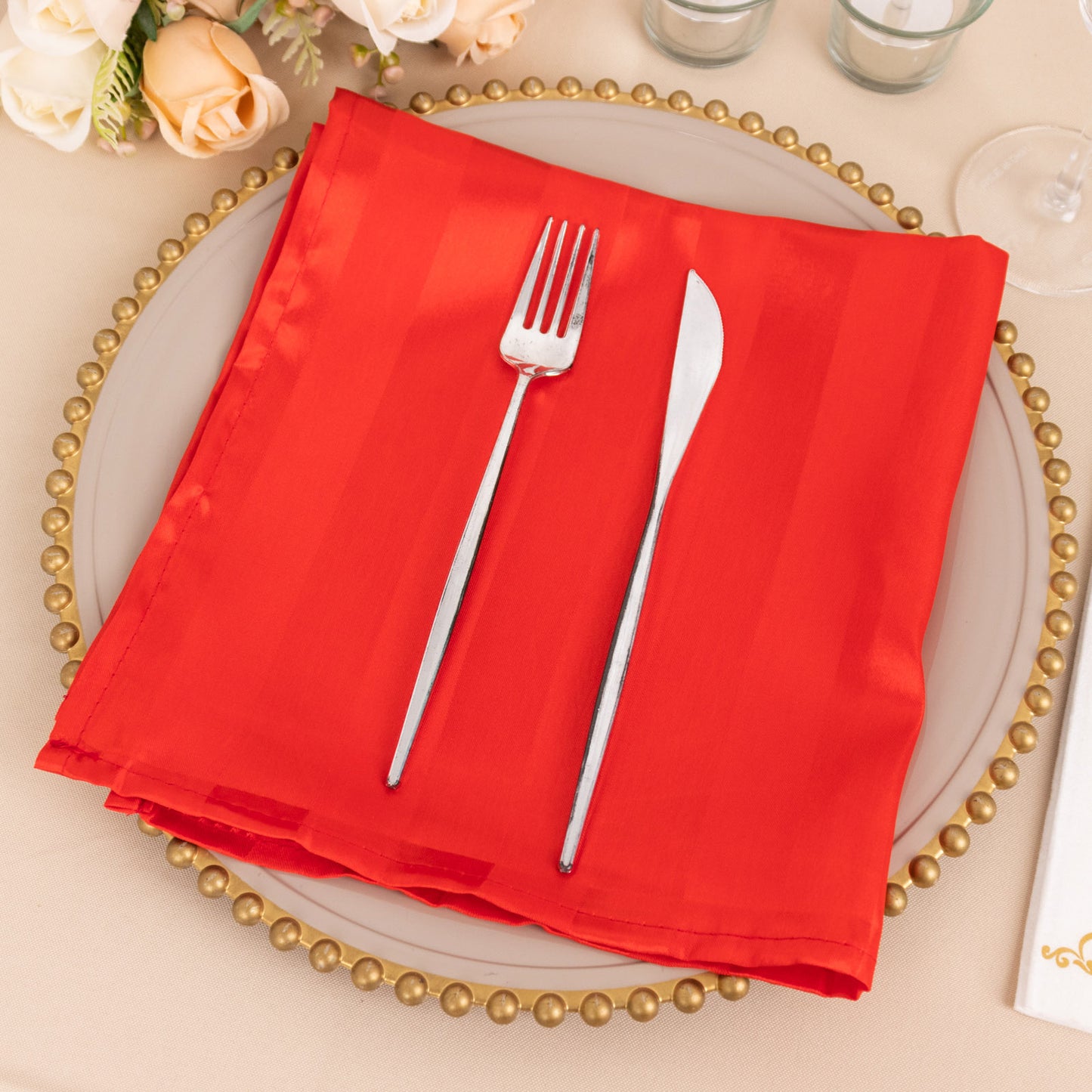 Red satin napkin on a decorative plate with silver utensils.
