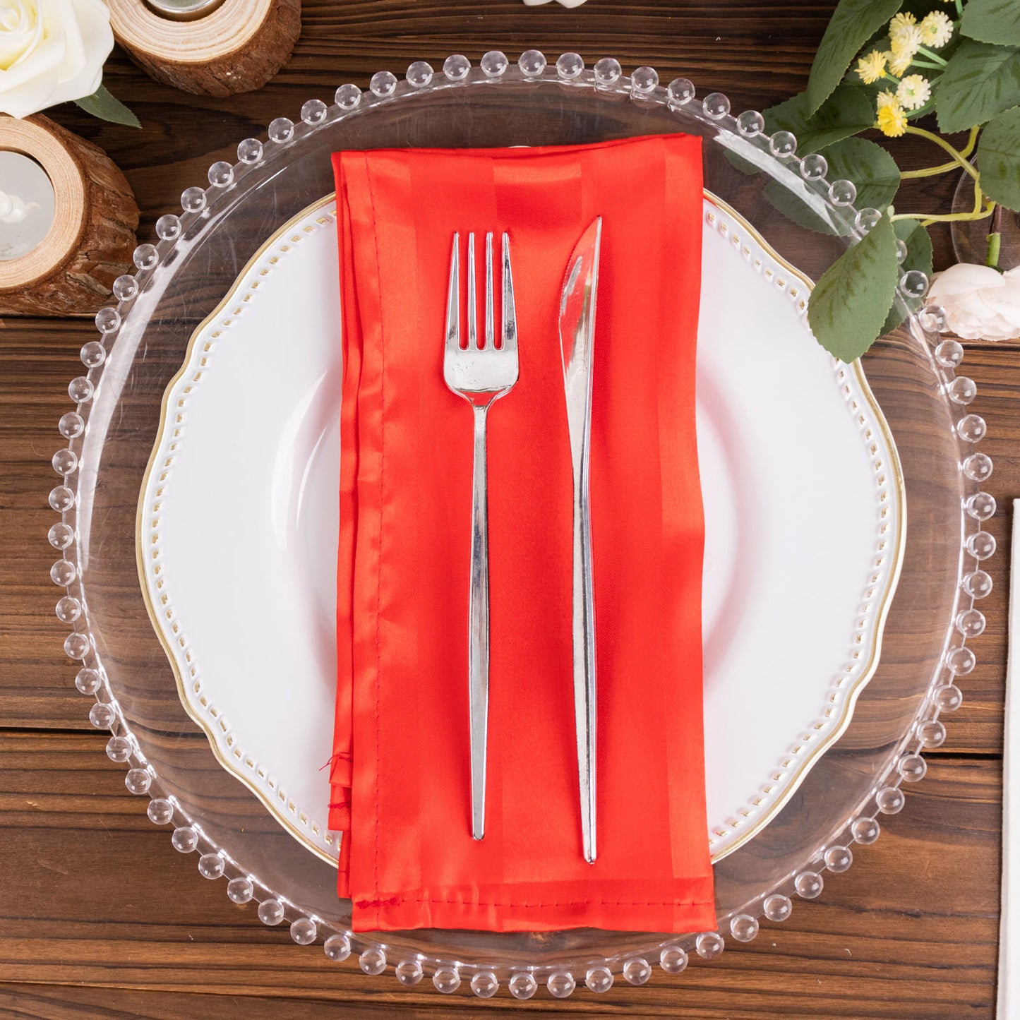 Red satin napkin on a decorative plate with silver cutlery.