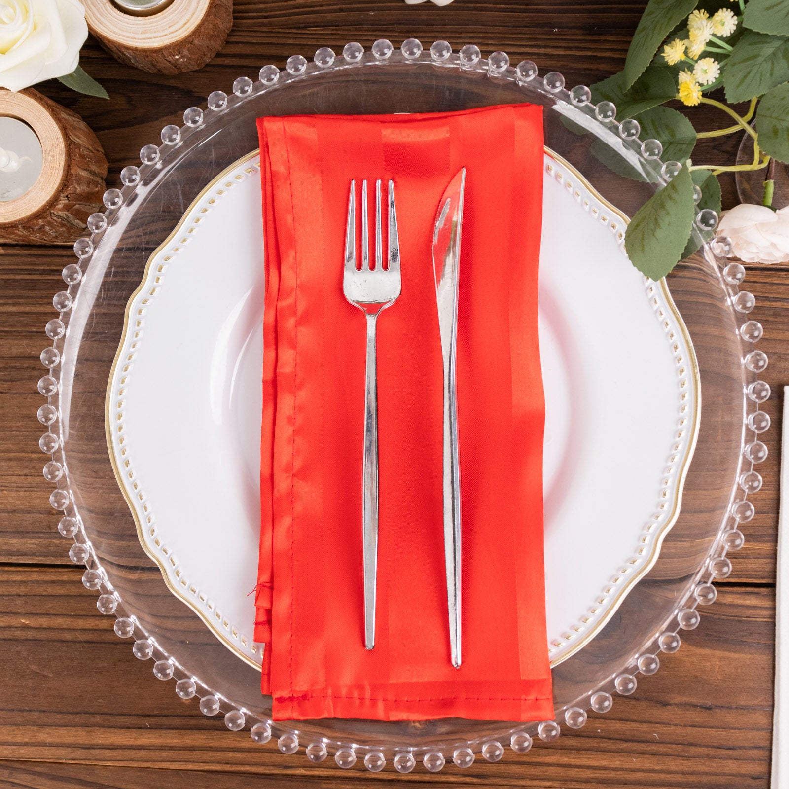 Red satin napkin on a decorative plate with silver cutlery.
