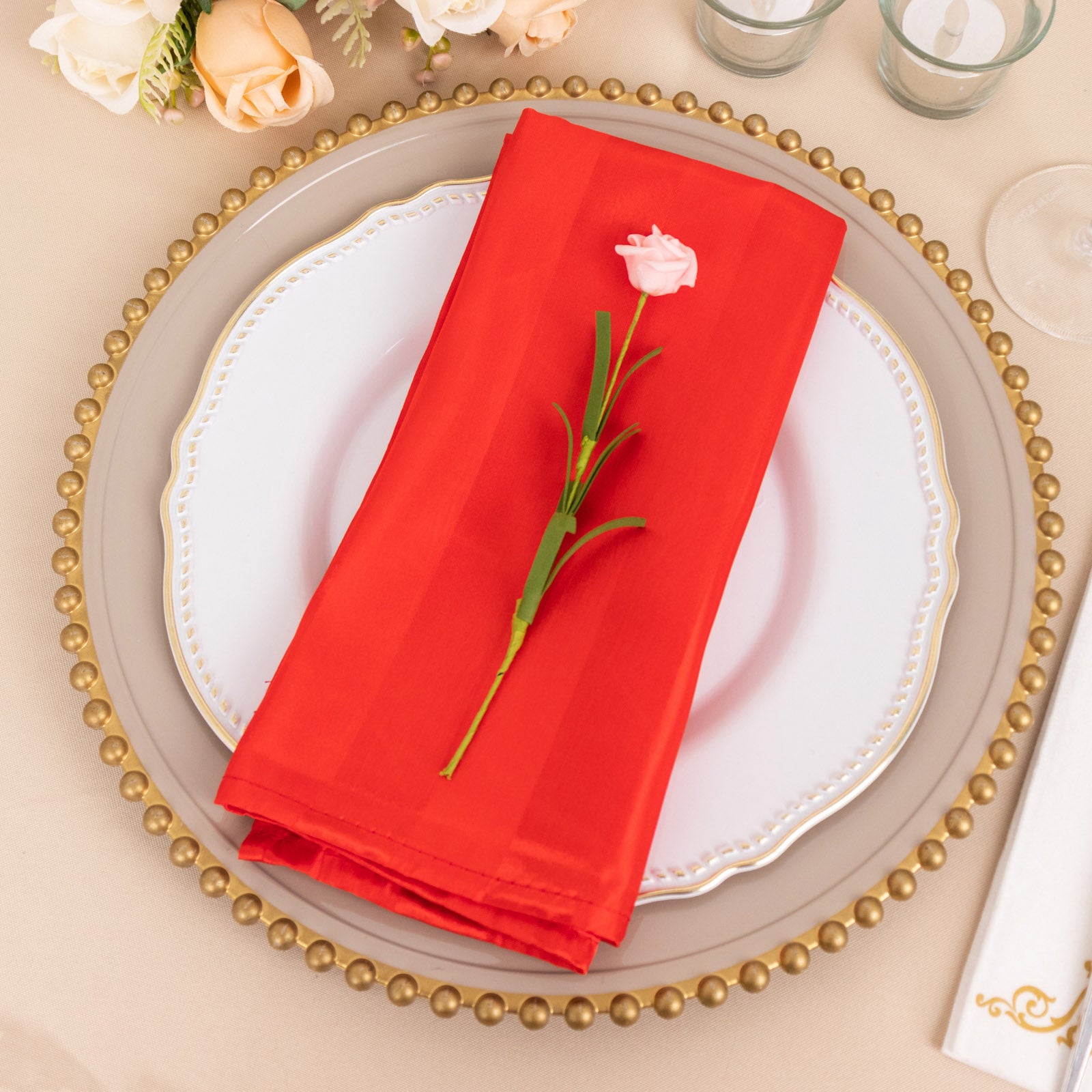 Red satin linen napkin on a decorative plate with a rose.