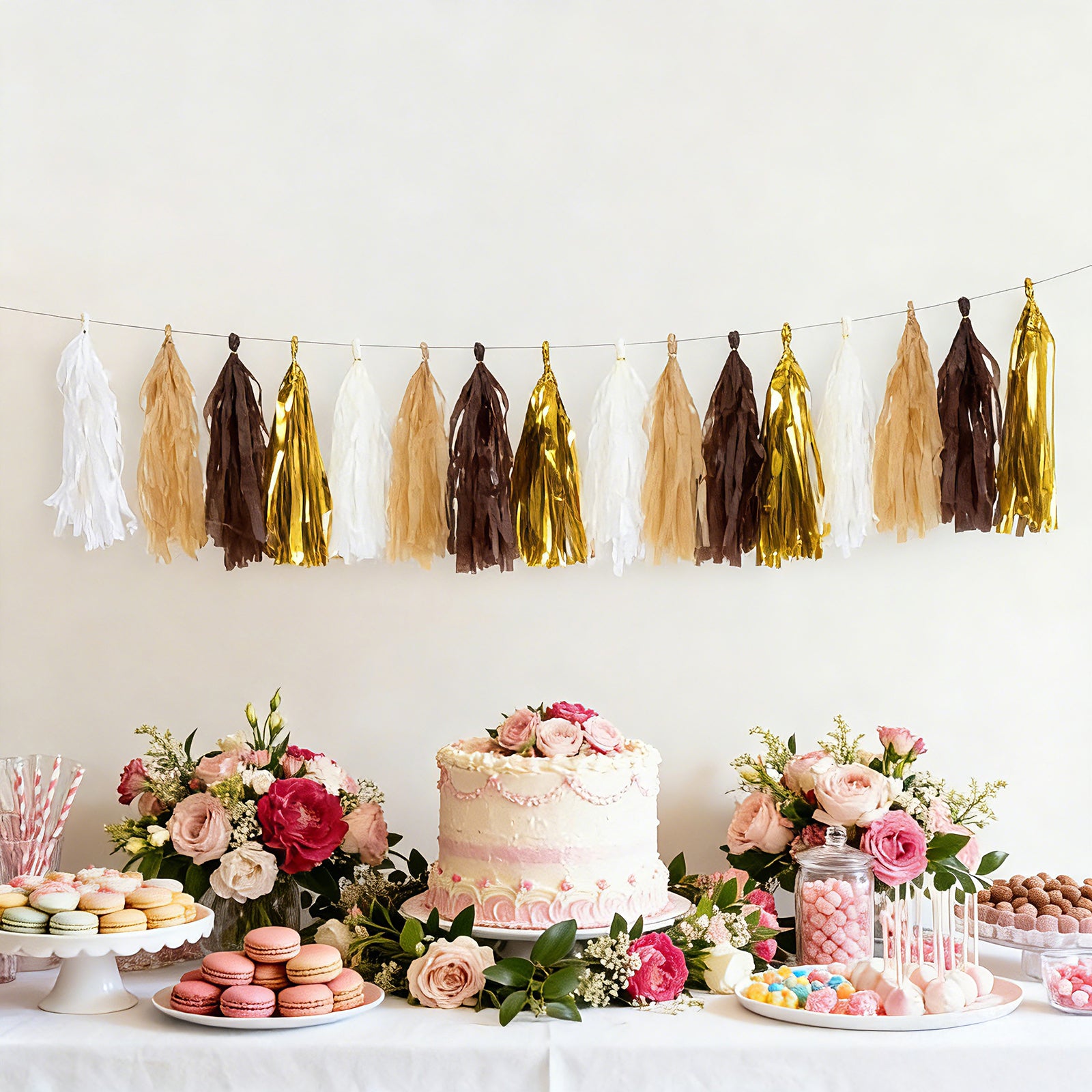 Gold and natural paper tassel garland banner decoration hanging above a cake and flowers.