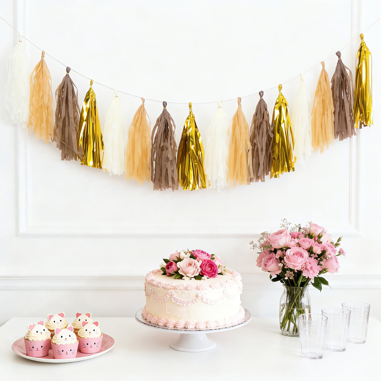 Natural and gold tassel garland banner decoration above a cake and flowers.