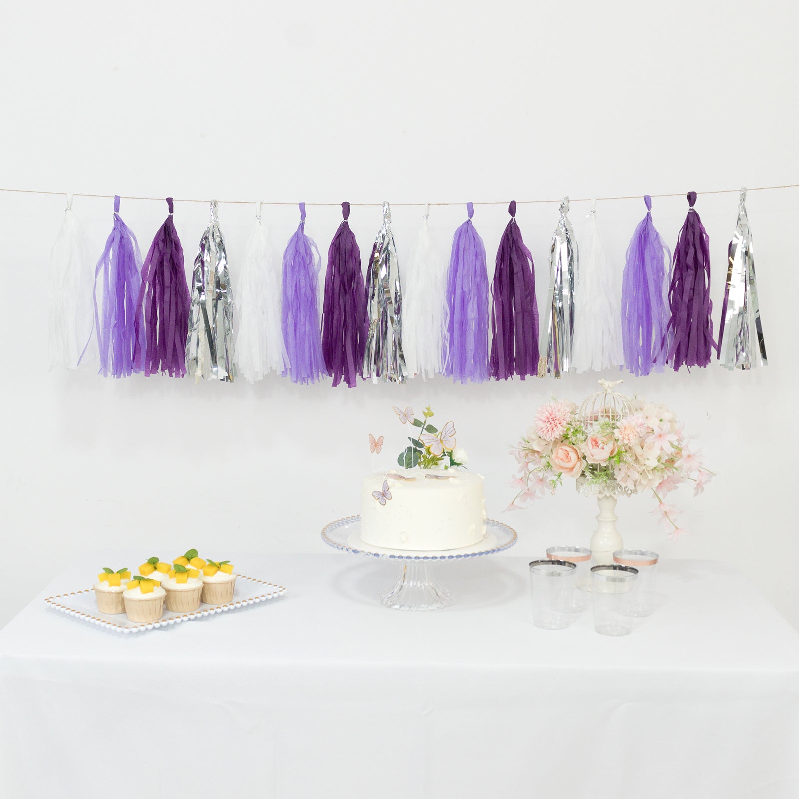 Purple and silver tassel garland banner decoration with cupcakes and cake.