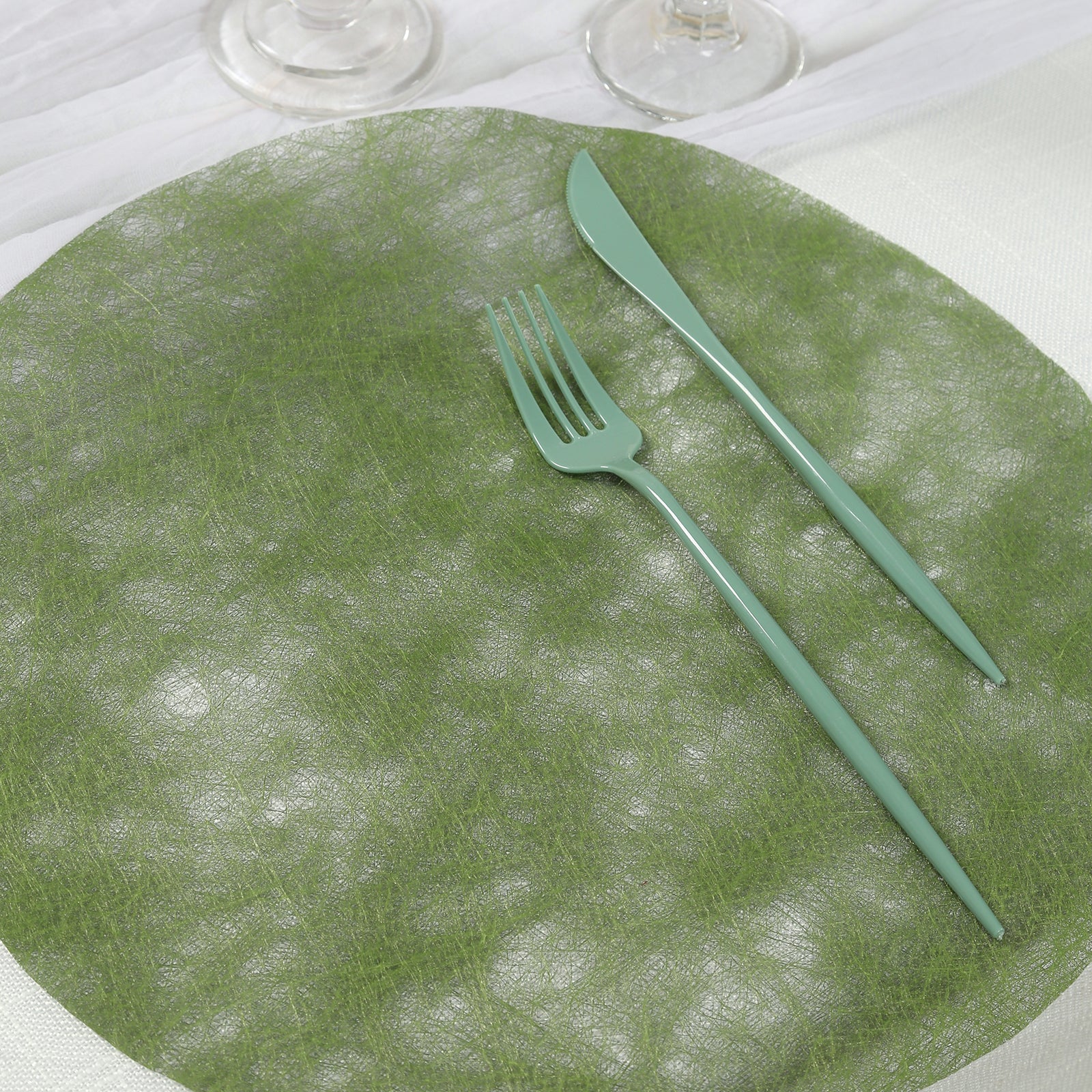 Olive green round placemat with fork and knife on a table setting.