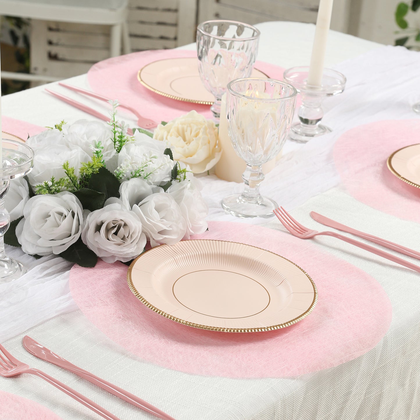 Pink disposable placemats on a dining table with elegant tableware and flowers.