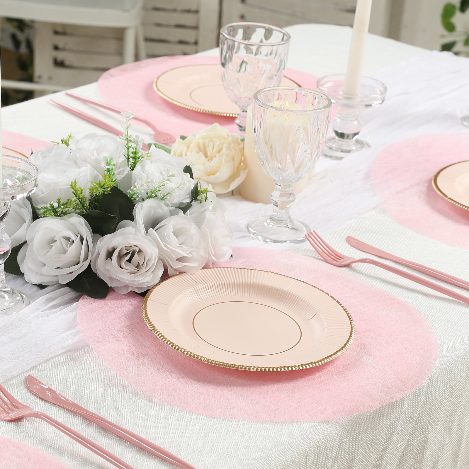 Pink disposable placemats on a dining table with elegant tableware and flowers.