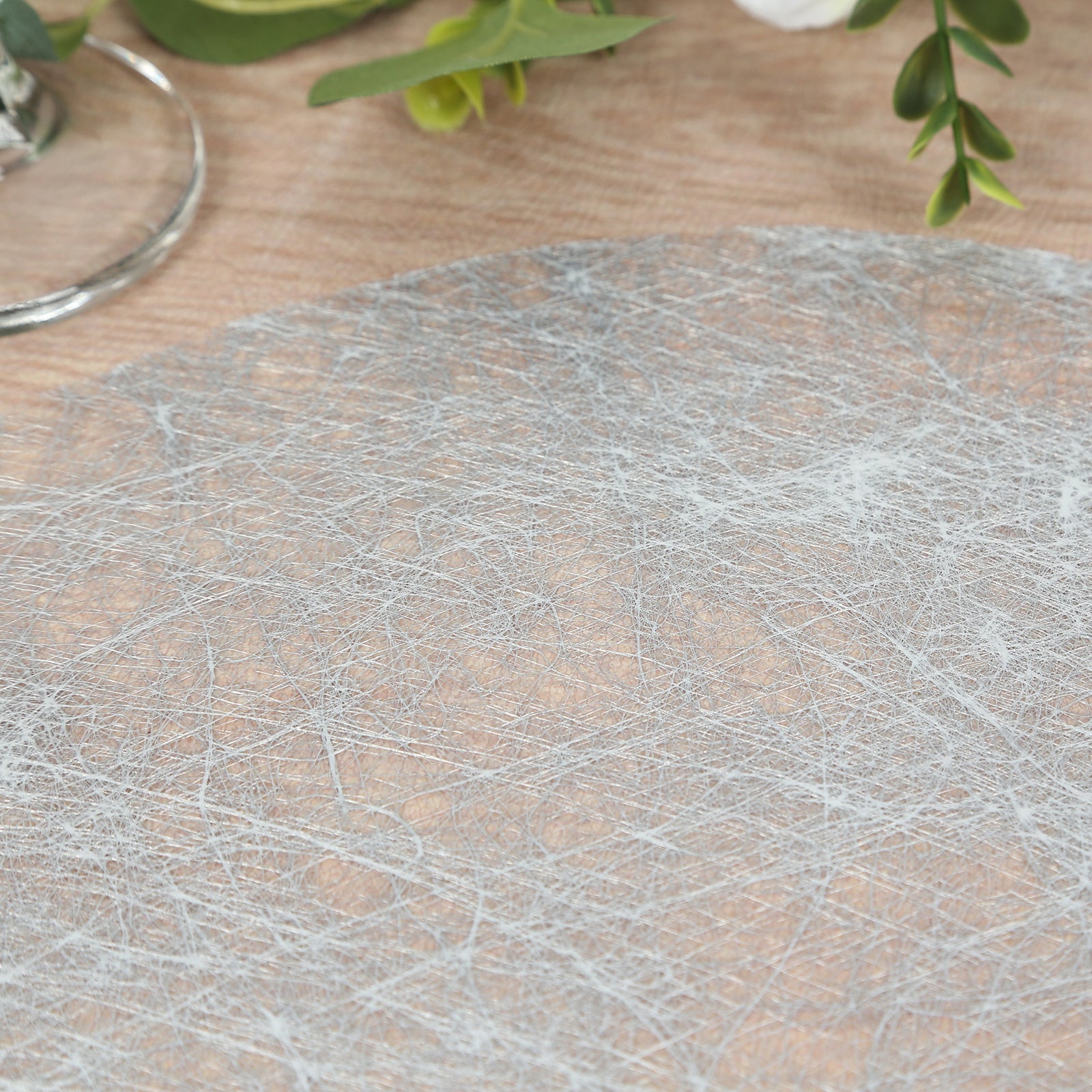 Metallic silver disposable round placemat on a wooden table.