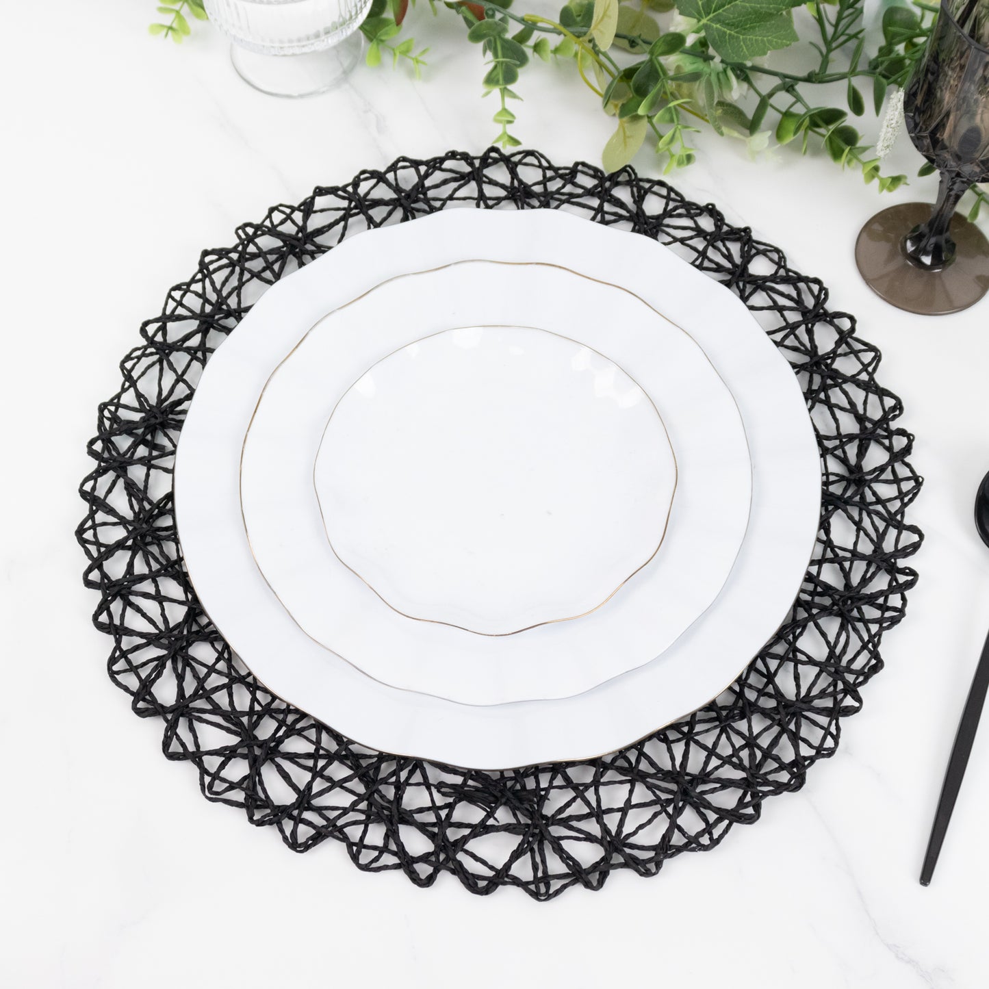 Black round woven fiber placemat with white plates on a marble table.