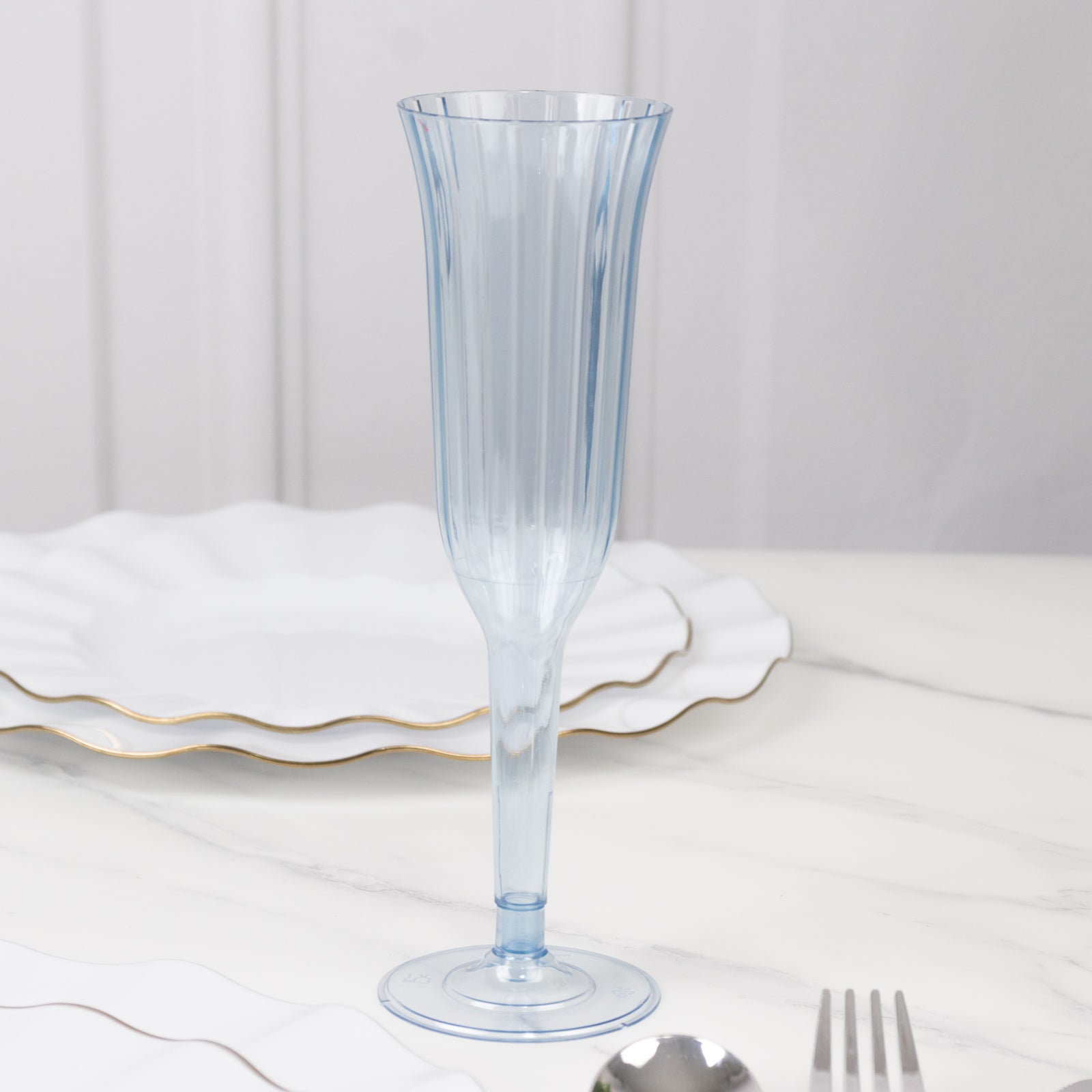 Dusty blue plastic champagne flute with a flared design on a marble surface.