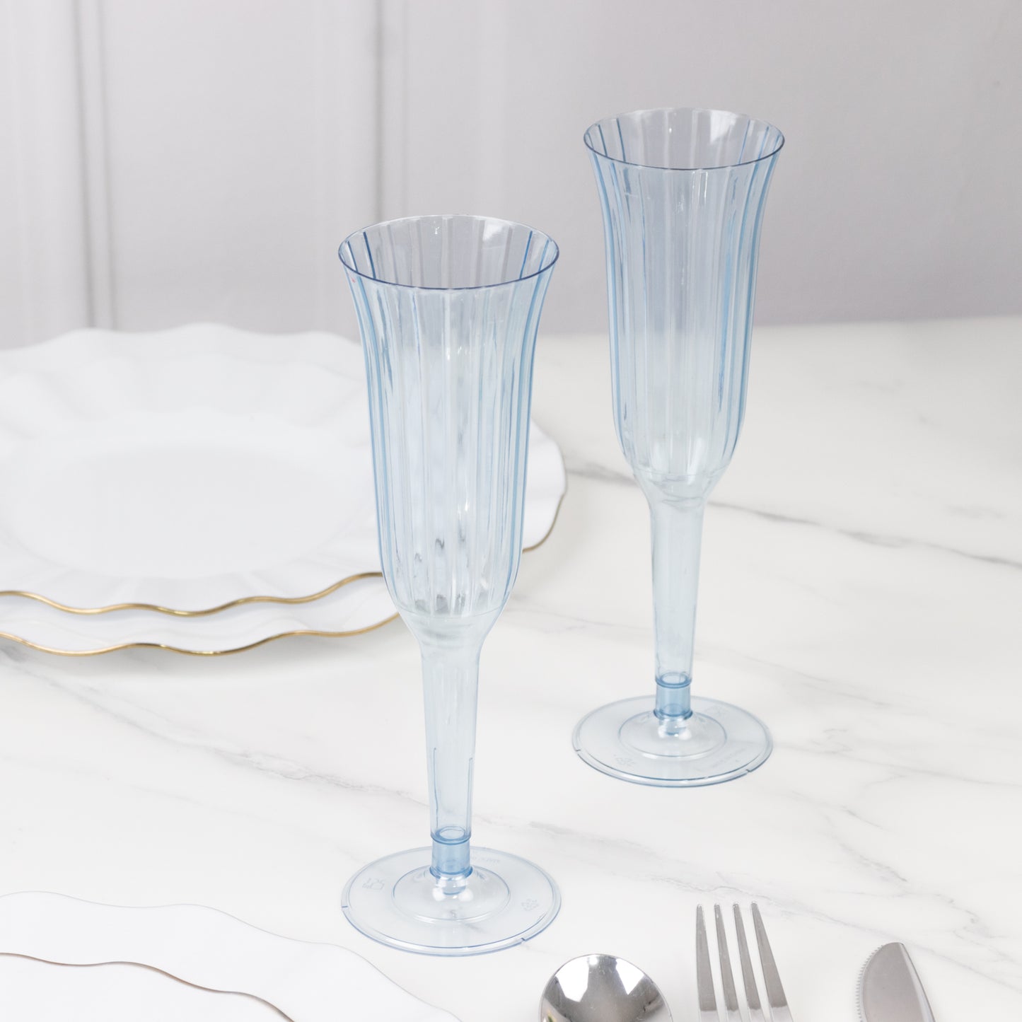 Transparent dusty blue flared disposable champagne flutes on a marble surface.