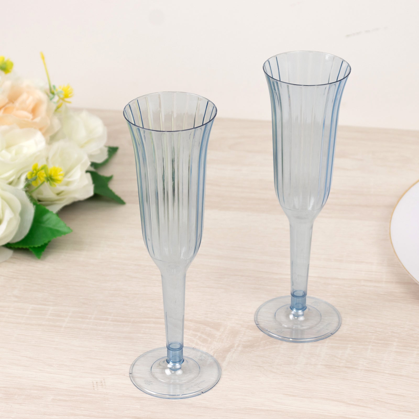 Transparent dusty blue plastic champagne flutes on a wooden surface.