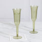 Dusty sage green plastic champagne flutes on a marble surface.
