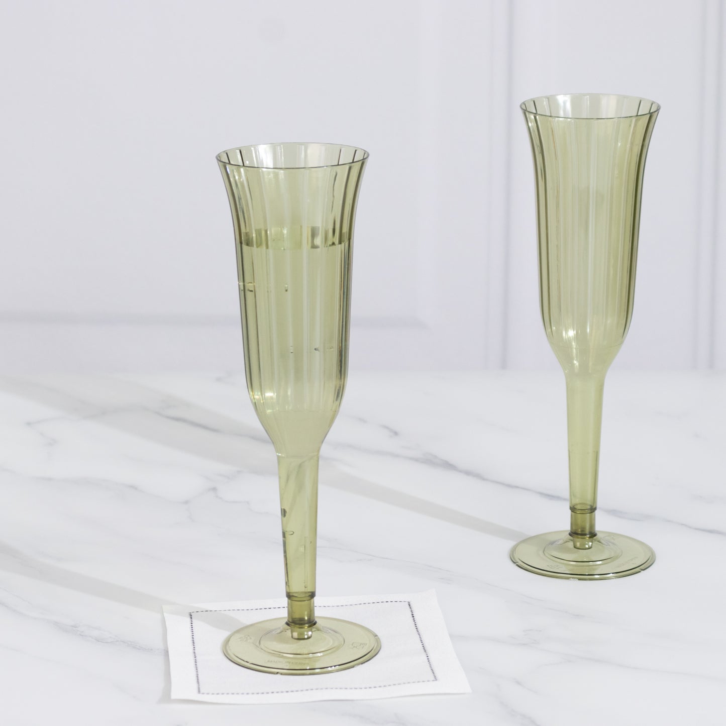 Dusty sage green plastic champagne flutes on a marble surface.