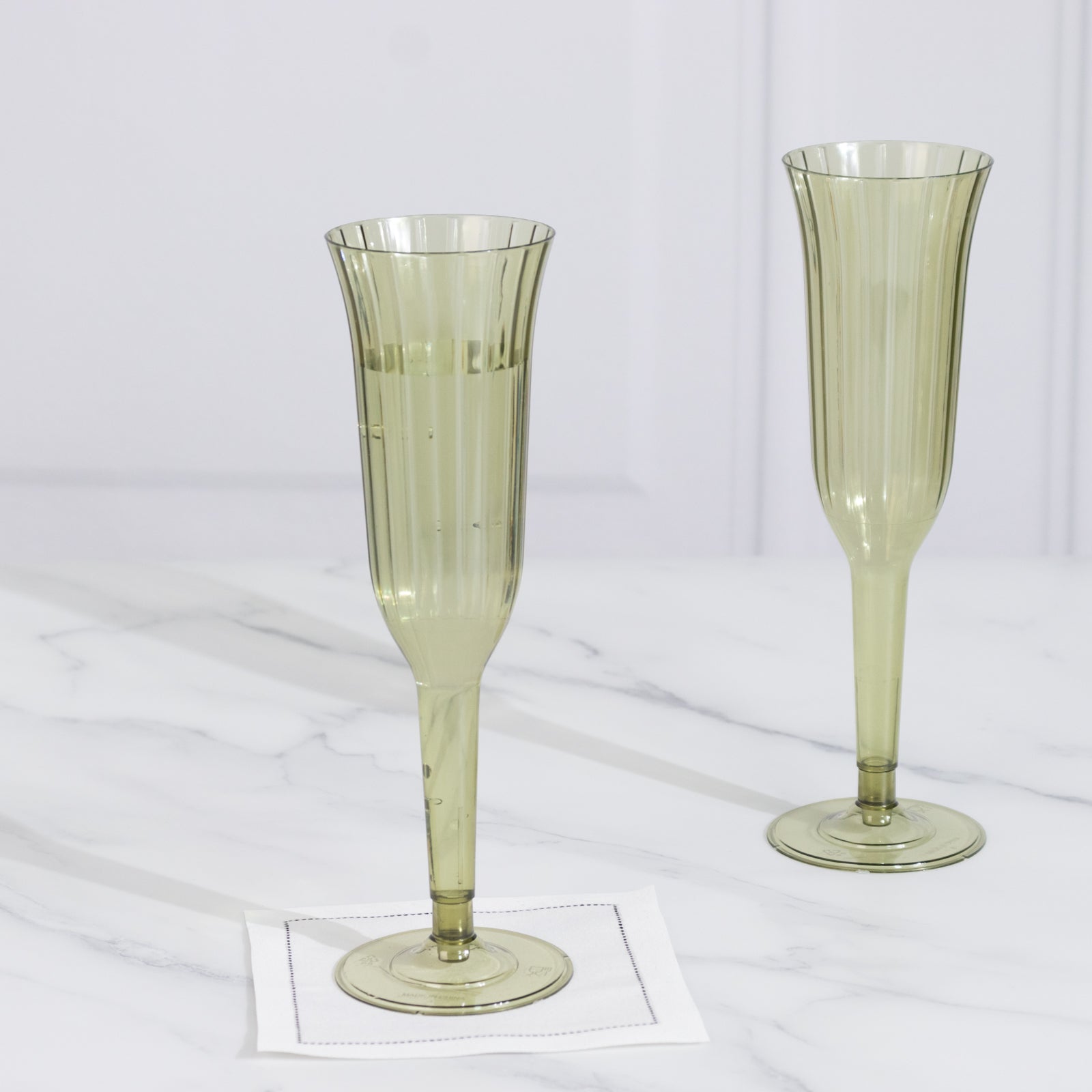 Dusty sage green plastic champagne flutes on a marble surface.