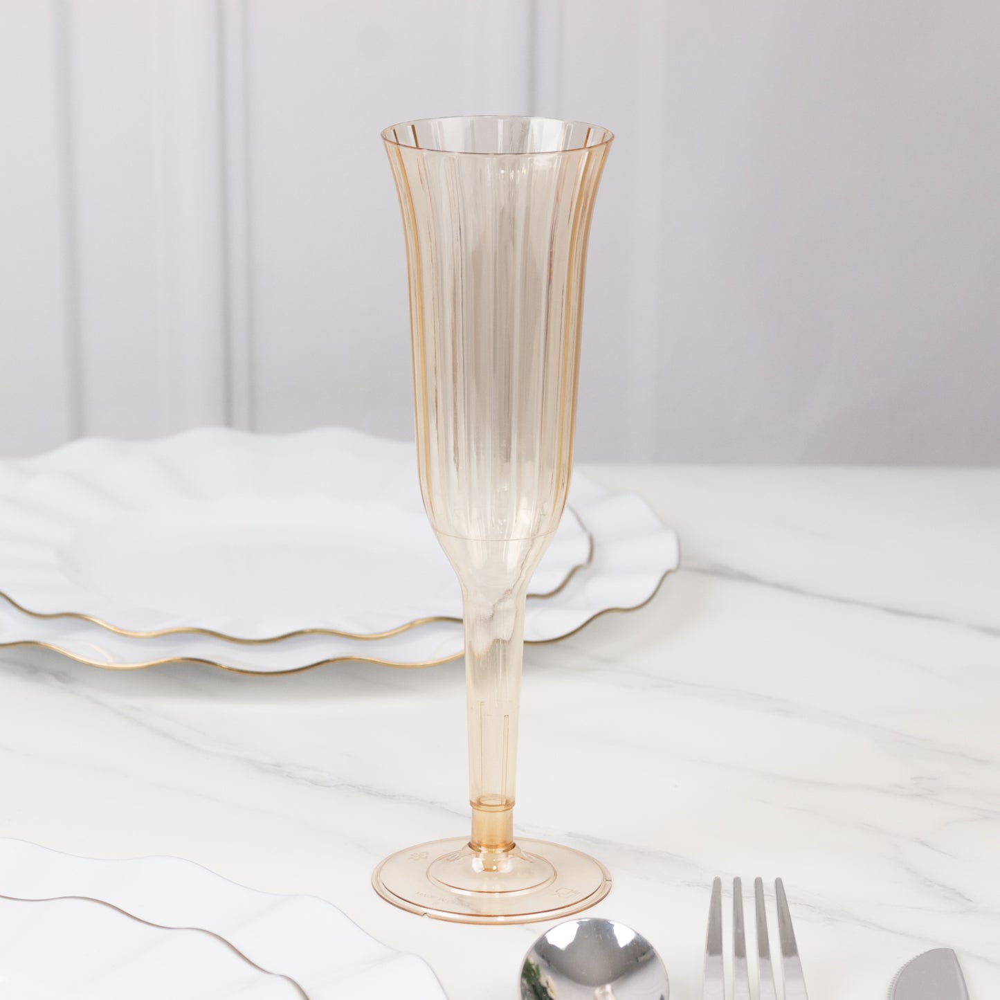 Transparent amber gold flared disposable champagne flute on a marble table.