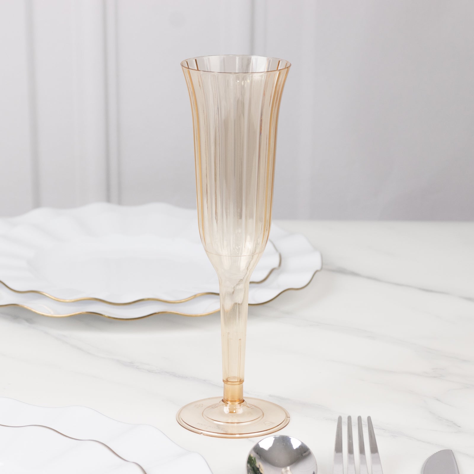 Transparent amber gold flared disposable champagne flute on a marble table.