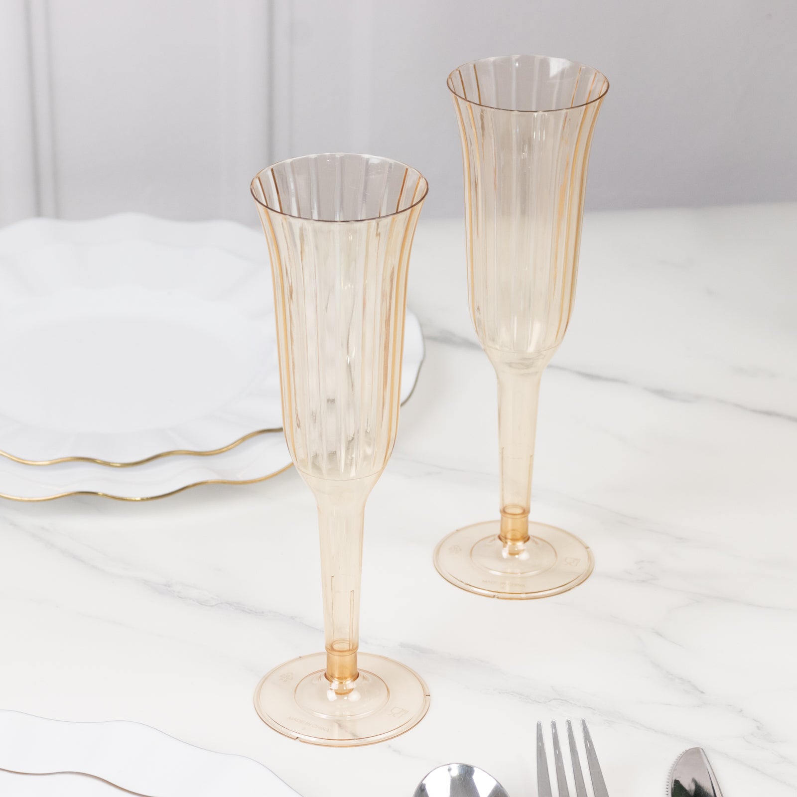 Transparent amber gold flared design plastic champagne flutes on a marble surface.