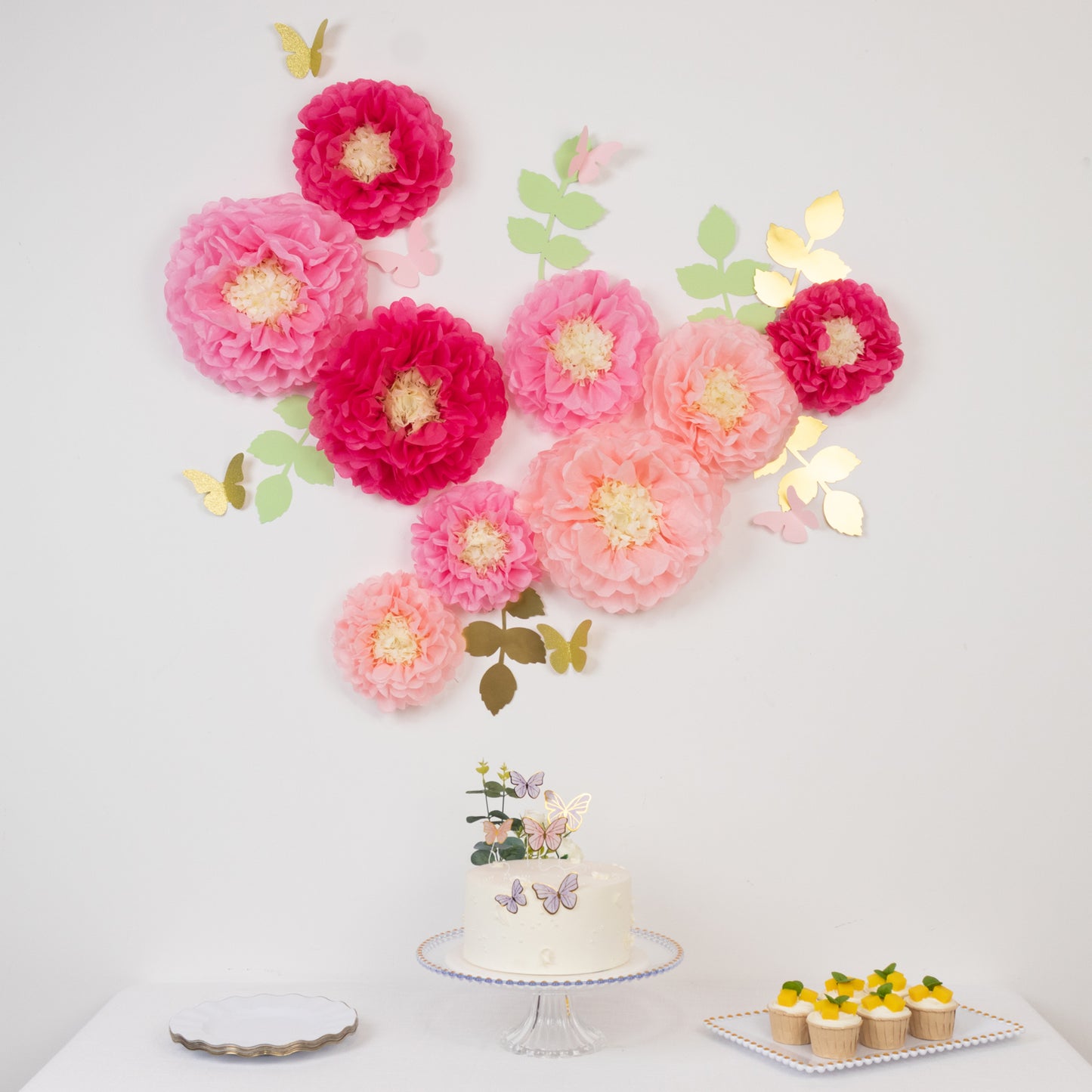 Blush pink tissue paper pom poms with butterflies and olive leaves wall decor.