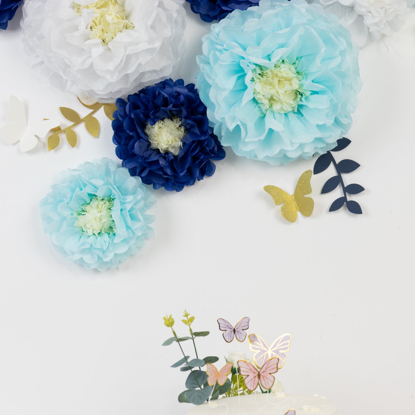 White and blue tissue paper flowers with butterflies and leaves for decor.
