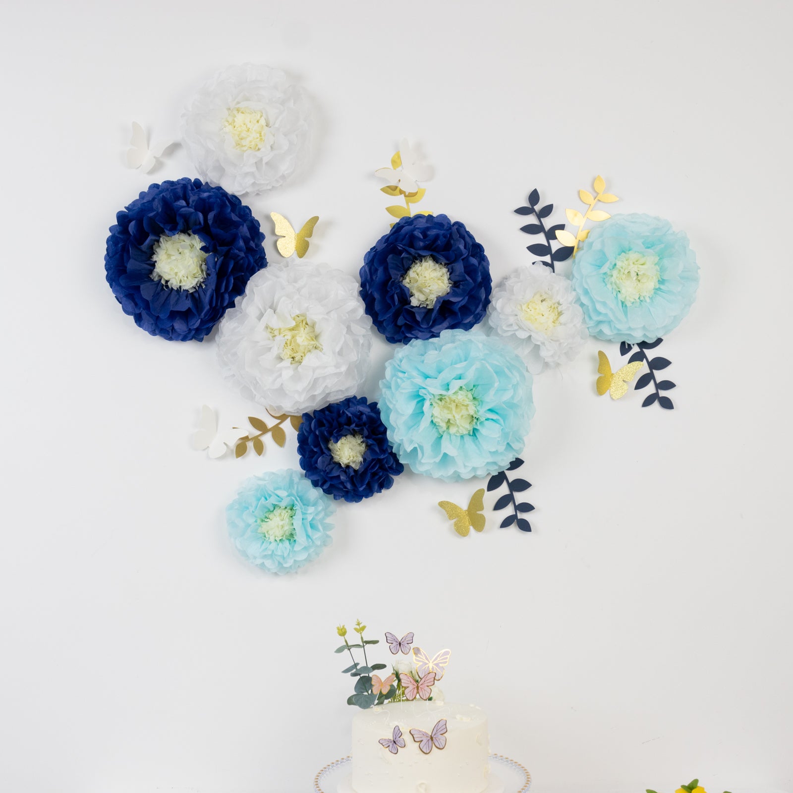 White and blue tissue paper flower pom poms wall decor with butterflies and leaves.