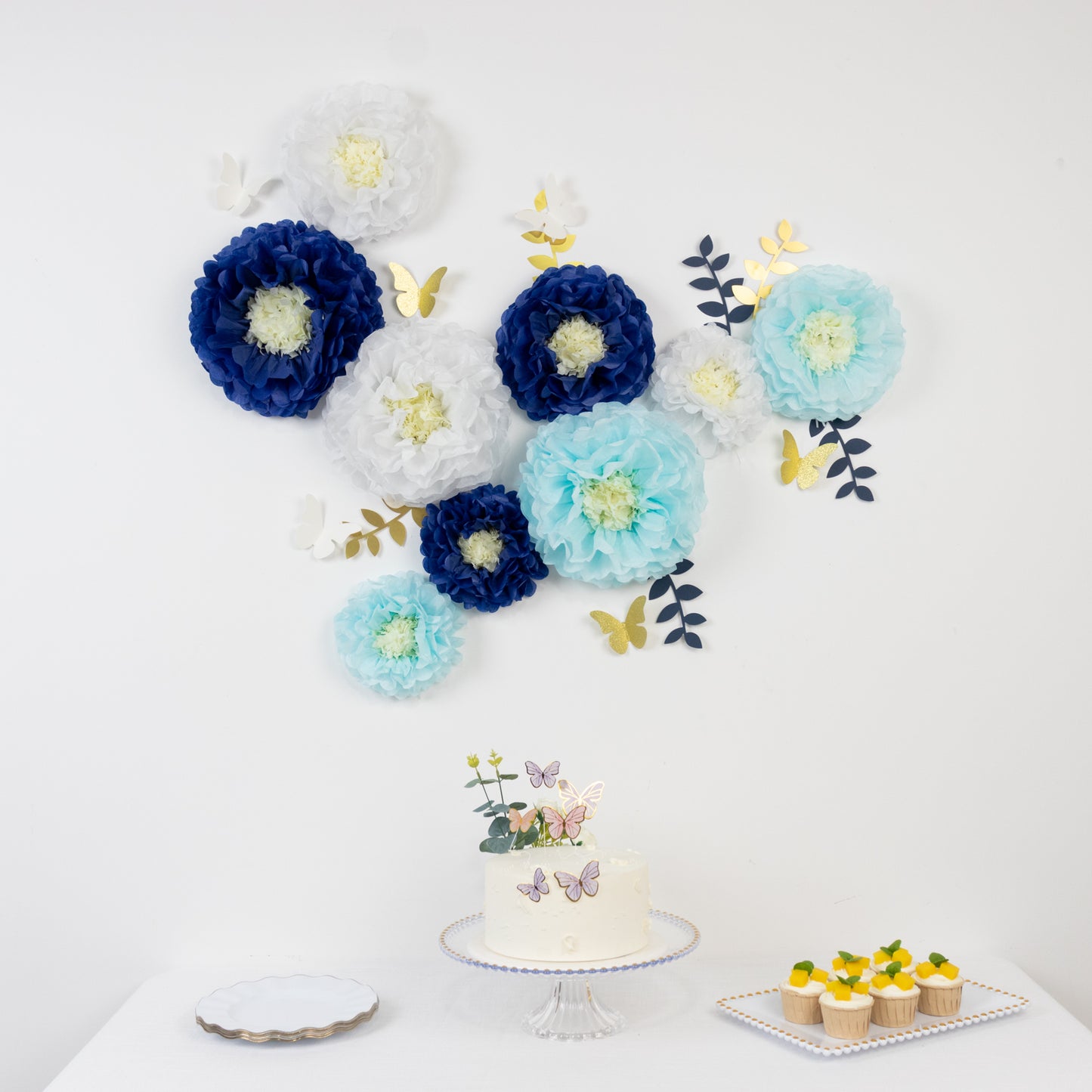 White and blue tissue paper flower pom poms with butterflies and olive leaves decor.