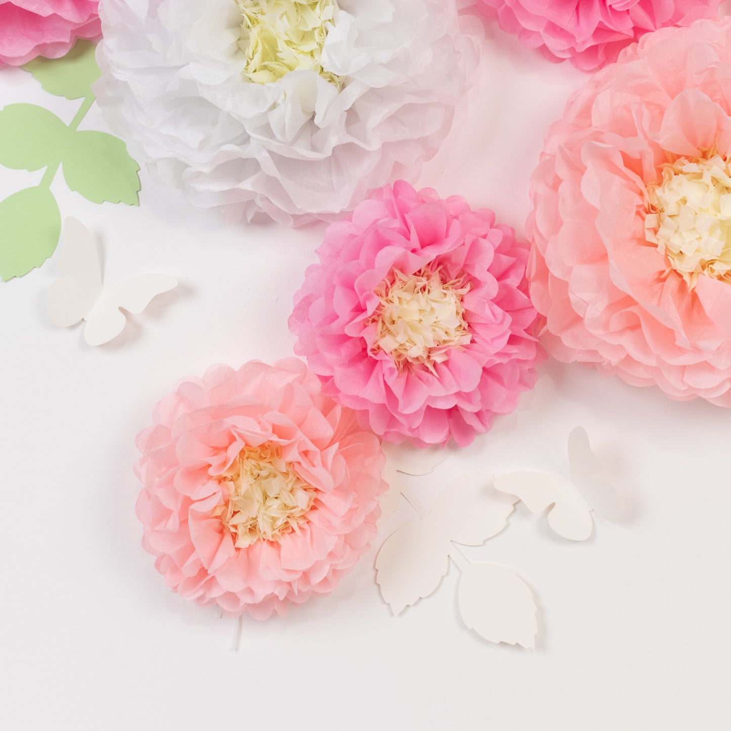 White and pink tissue paper flower decor with butterflies and leaves.