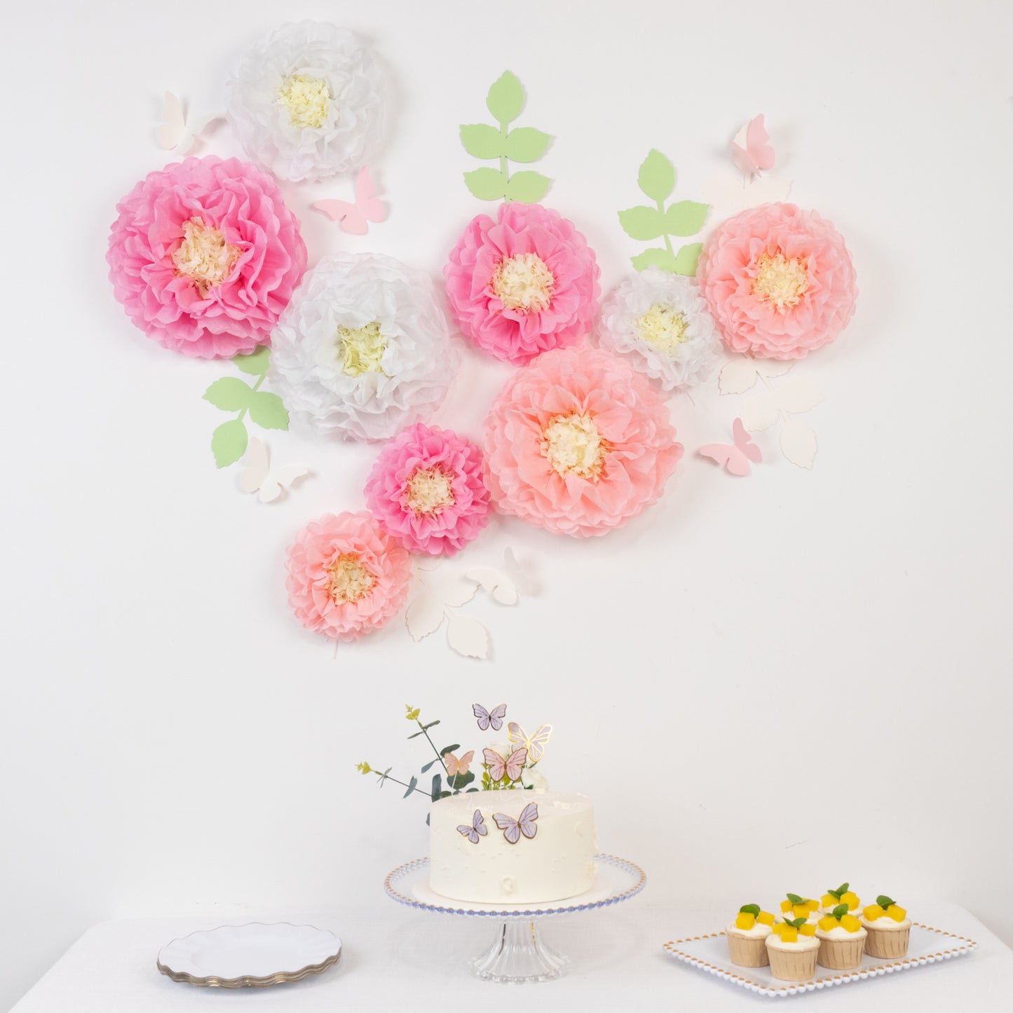 White and pink tissue paper flower pom poms with butterflies and leaves decor.