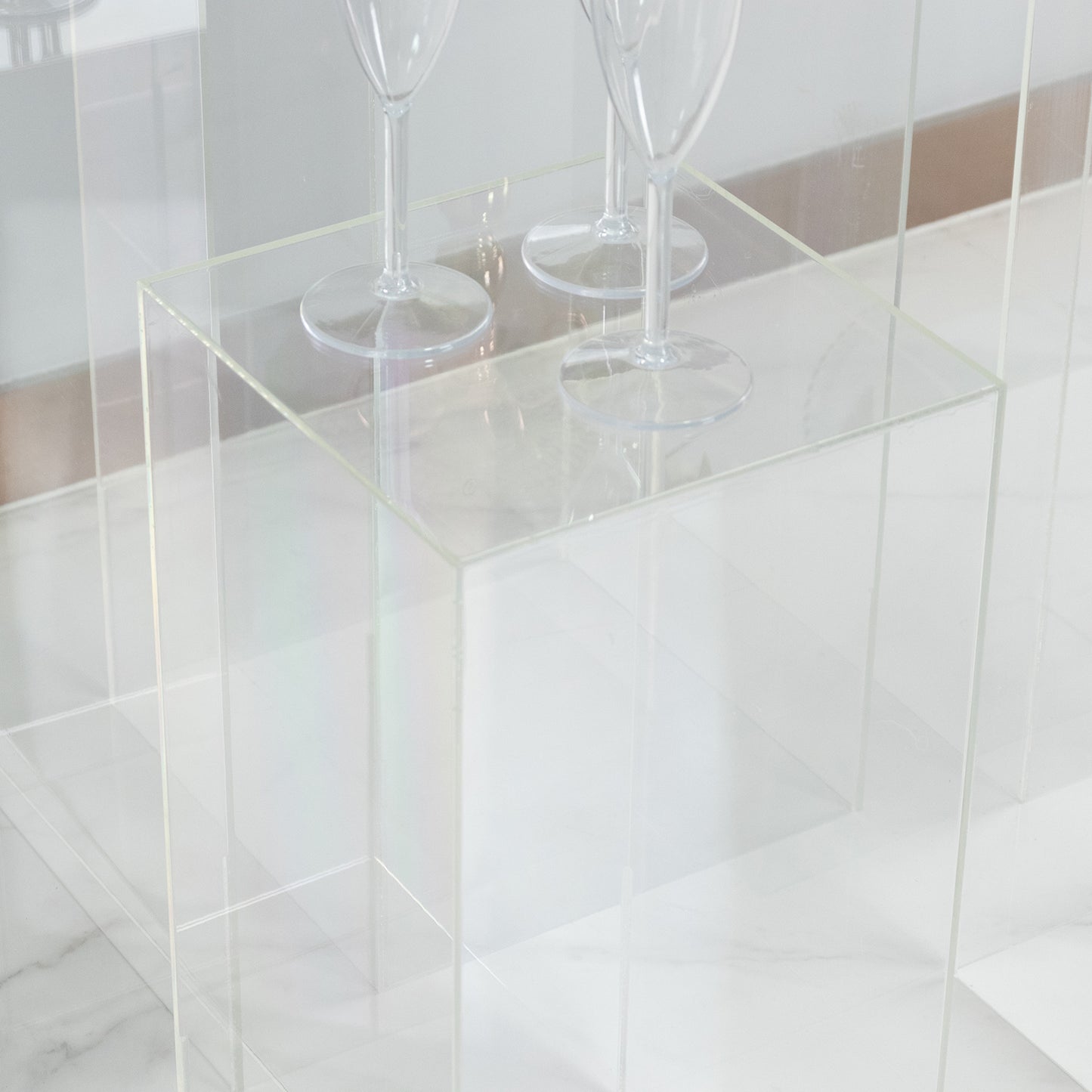 Clear acrylic pedestal stands displayed on a marble surface with wine glasses.