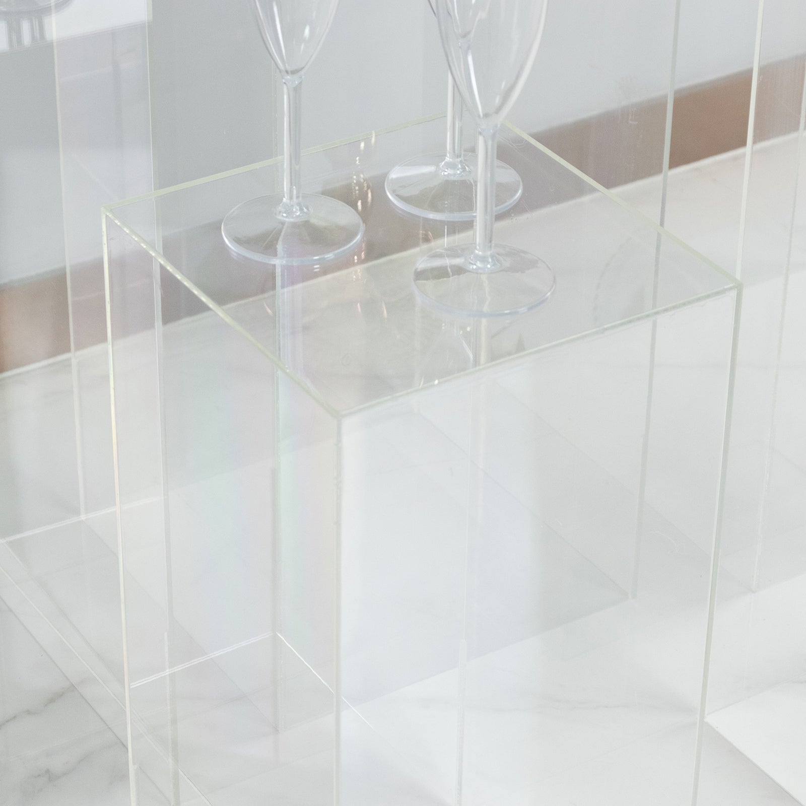 Clear acrylic pedestal stands displayed on a marble surface with wine glasses.
