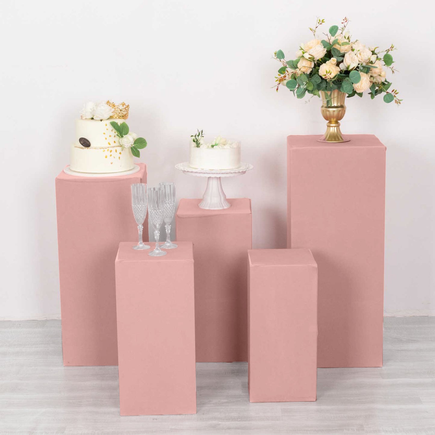 Dusty rose spandex pedestal stand covers in a stylish arrangement with floral decor.