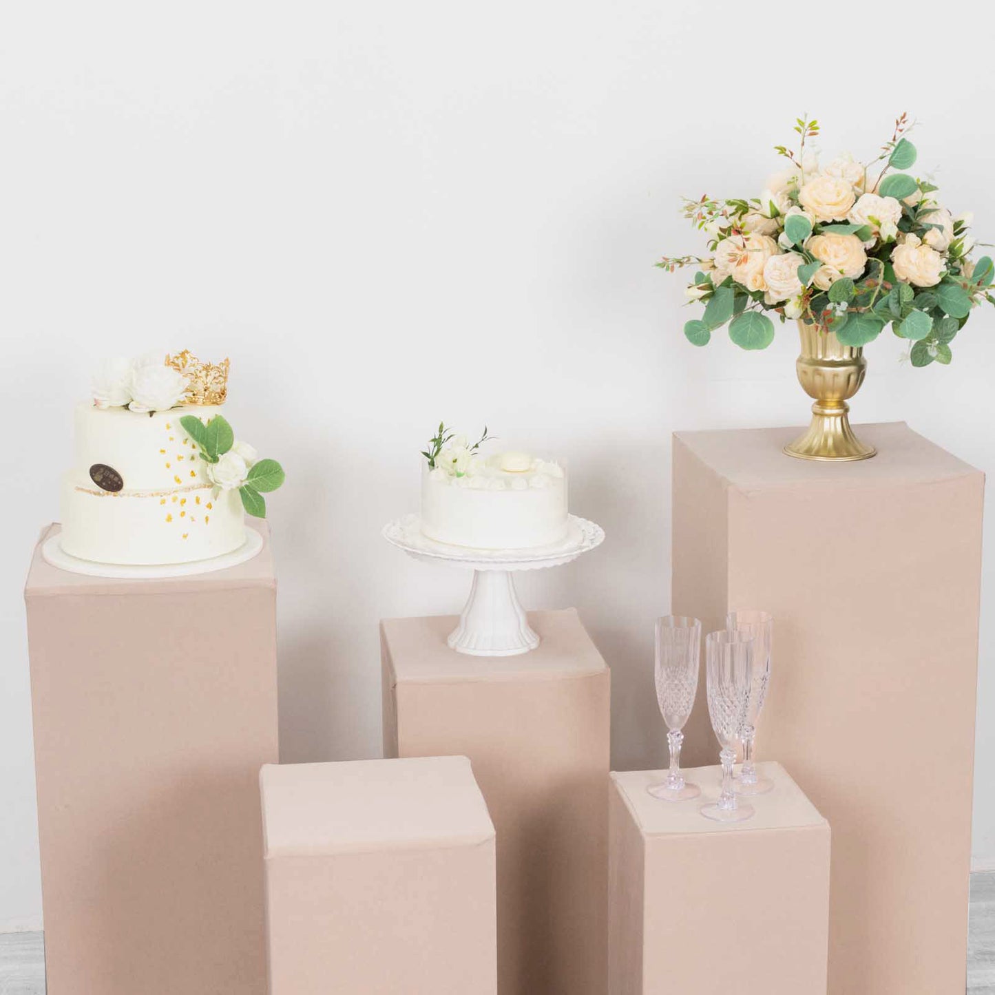 Nude spandex pedestal stand covers on display with floral arrangements and cake.