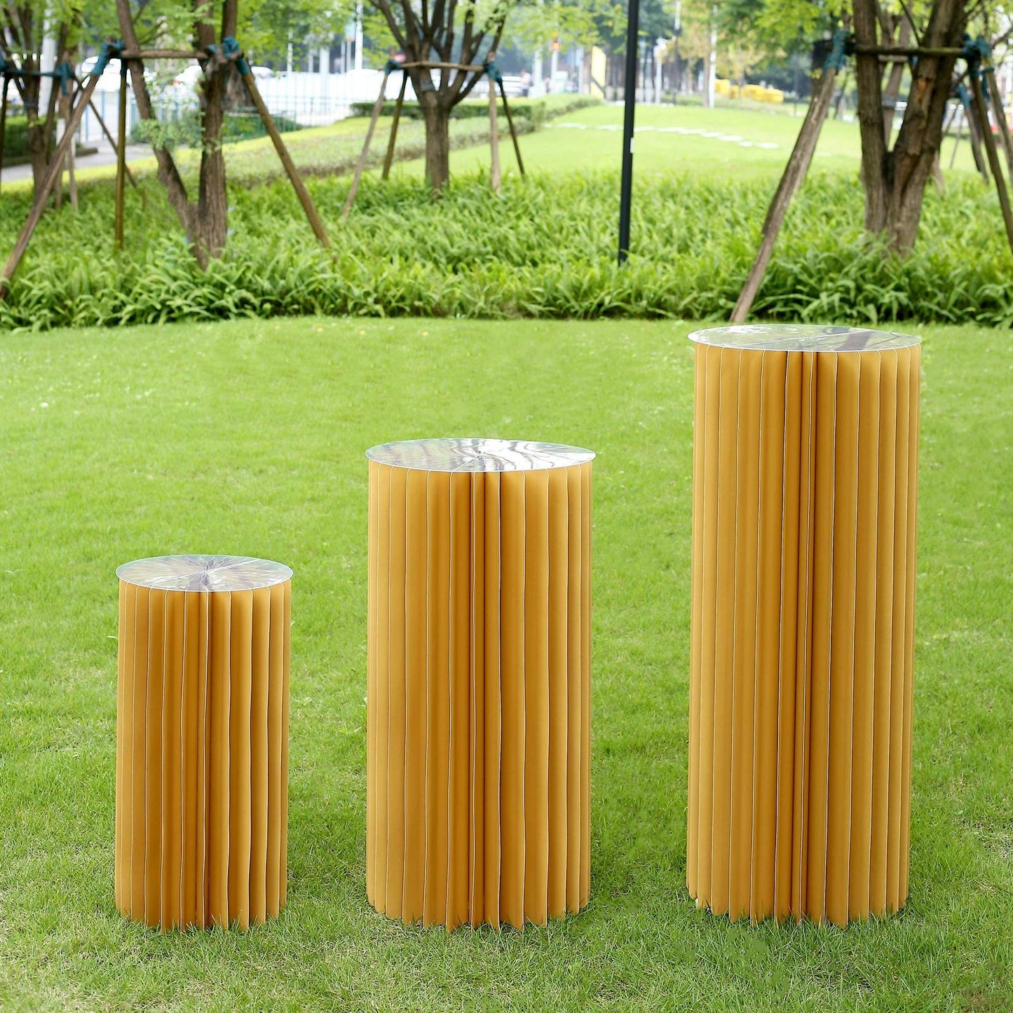 Gold cylinder display column stand set in an outdoor setting.