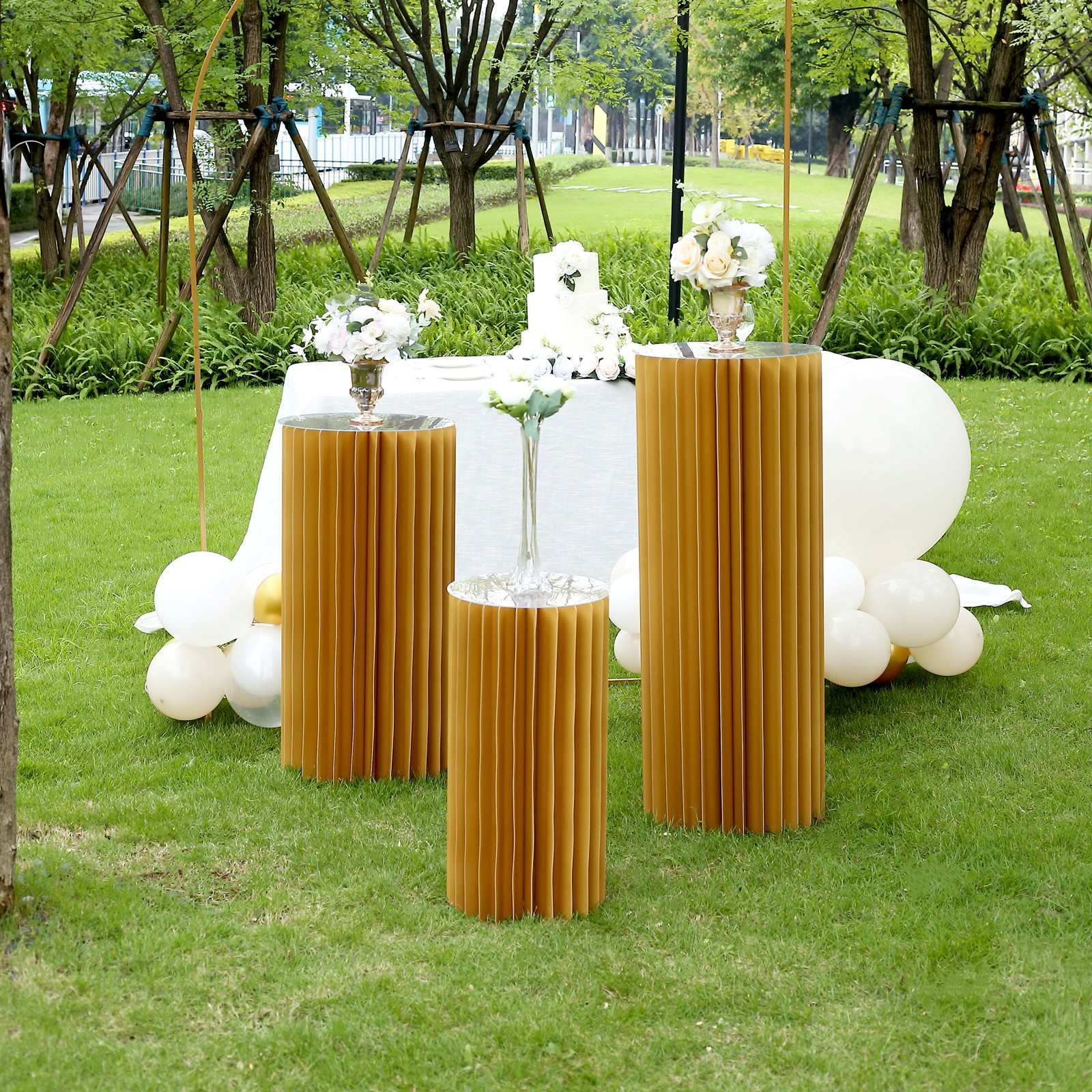 24" gold cylinder display column stand in a garden setting.
