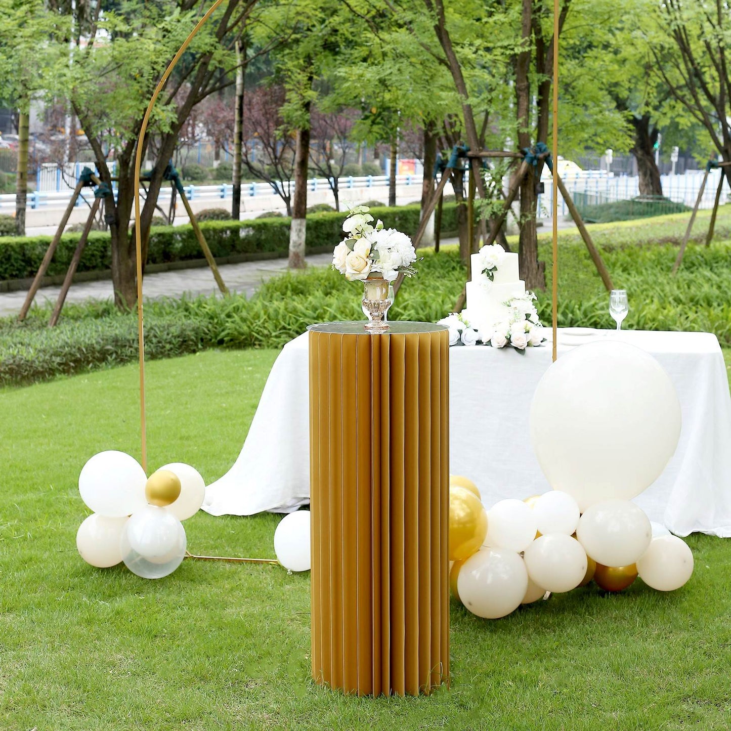 Gold cylinder display column stand in a garden setting.