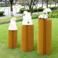 Gold cylinder display column stand with top plate in outdoor setting.