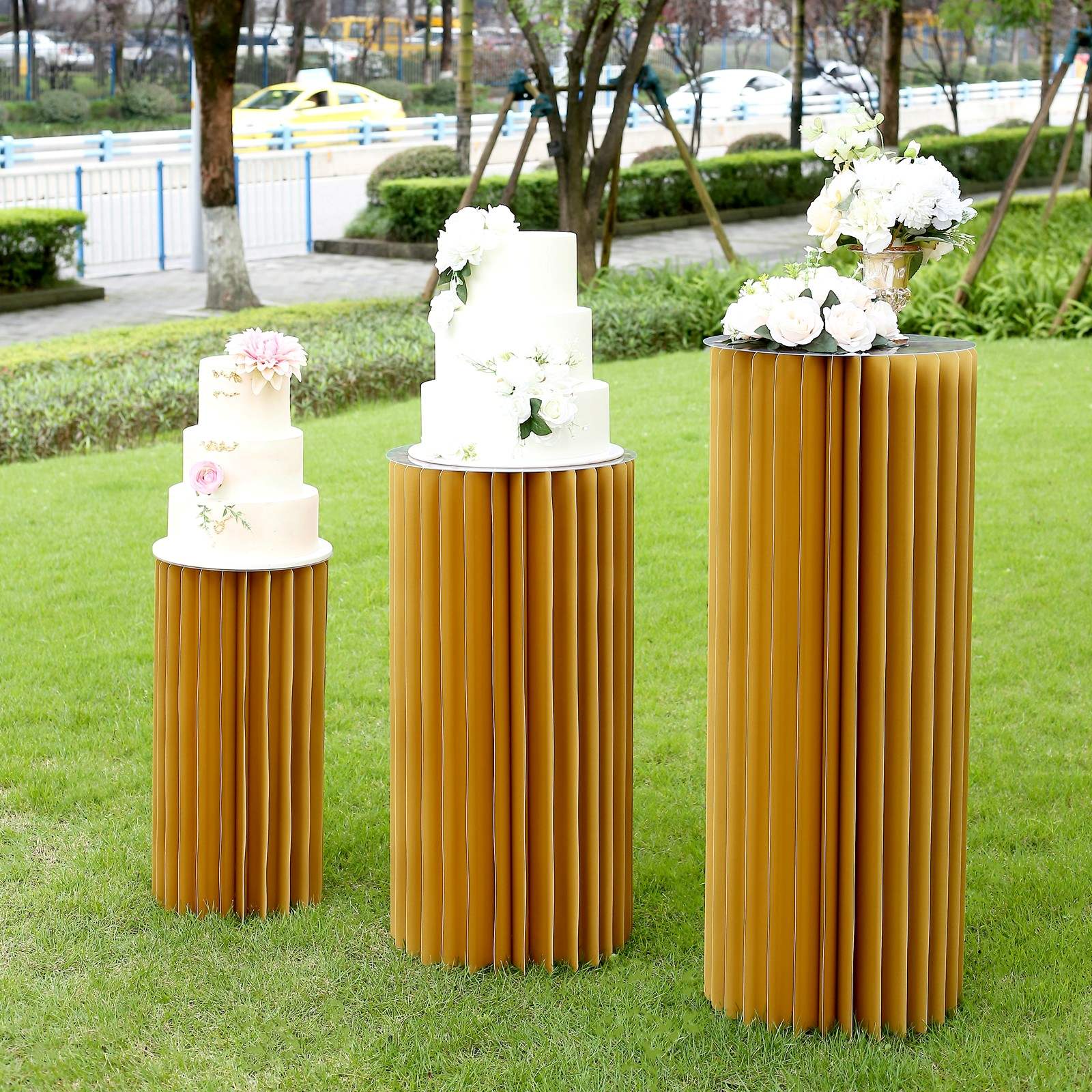 Gold cylinder display column stand with top plate in outdoor setting.