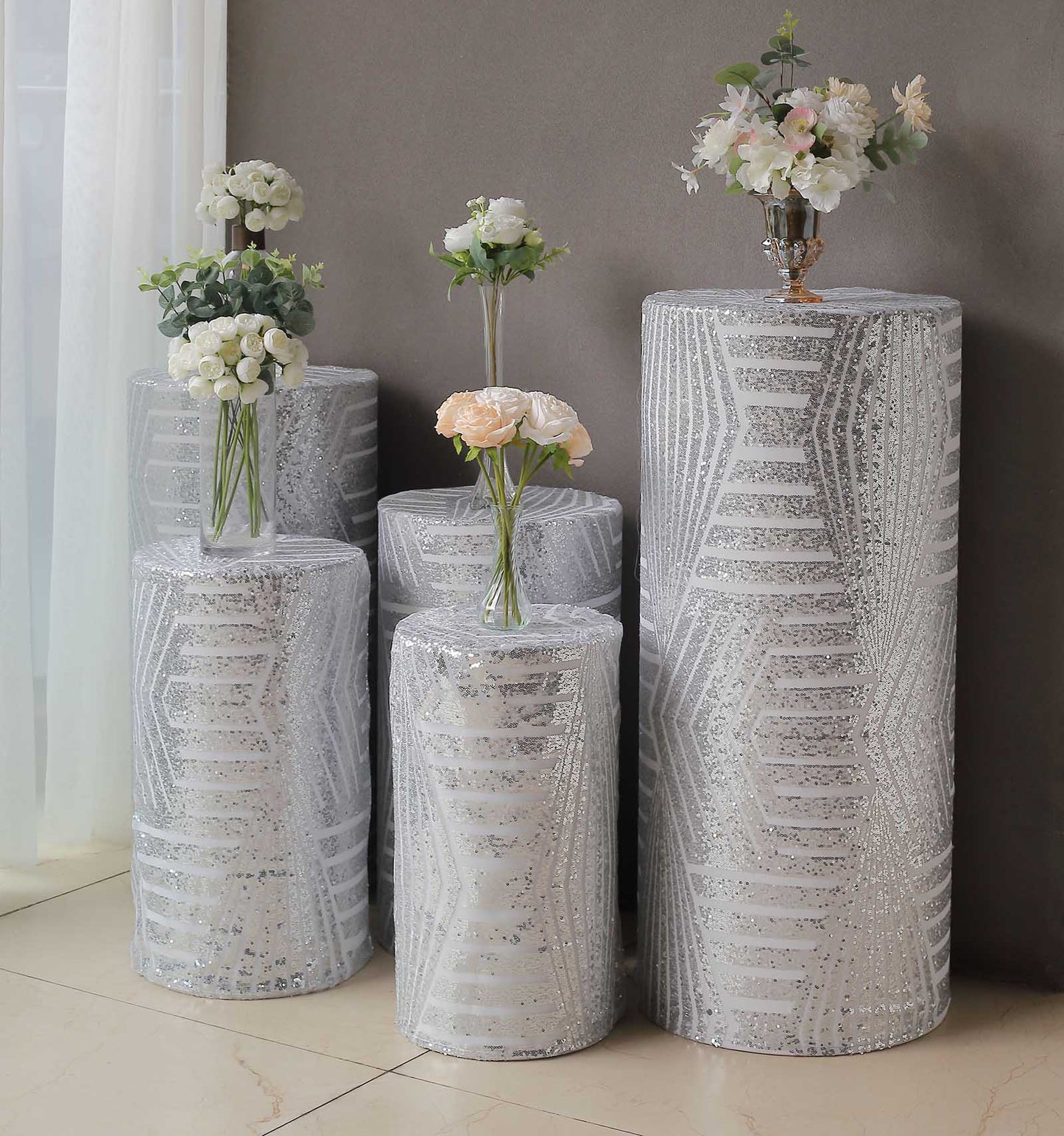 Silver sequin mesh pedestal stand covers with geometric pattern and floral arrangements.