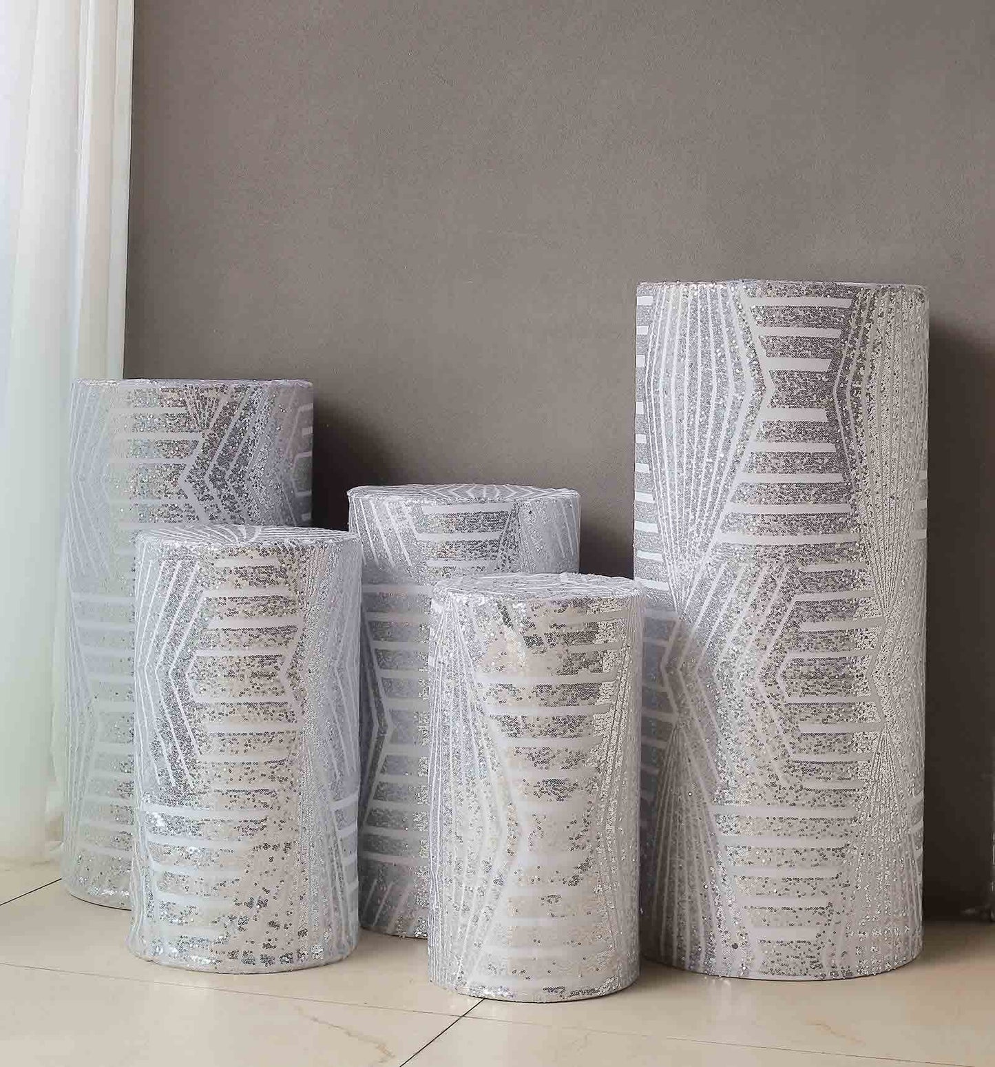 Set of 5 silver sequin mesh cylinder pedestal stand covers with geometric pattern.