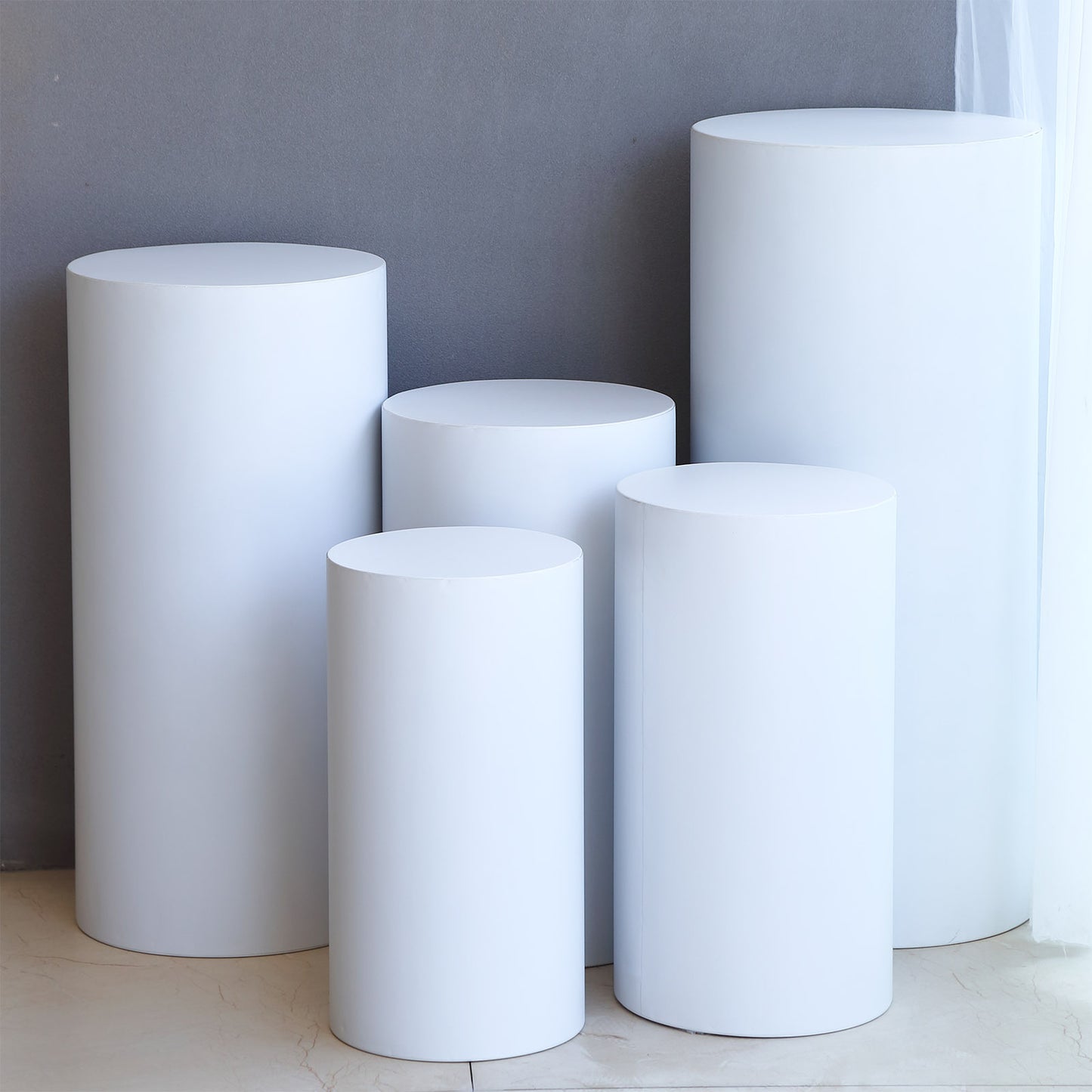 Set of 5 white metal cylinder pillar stands for wedding display.